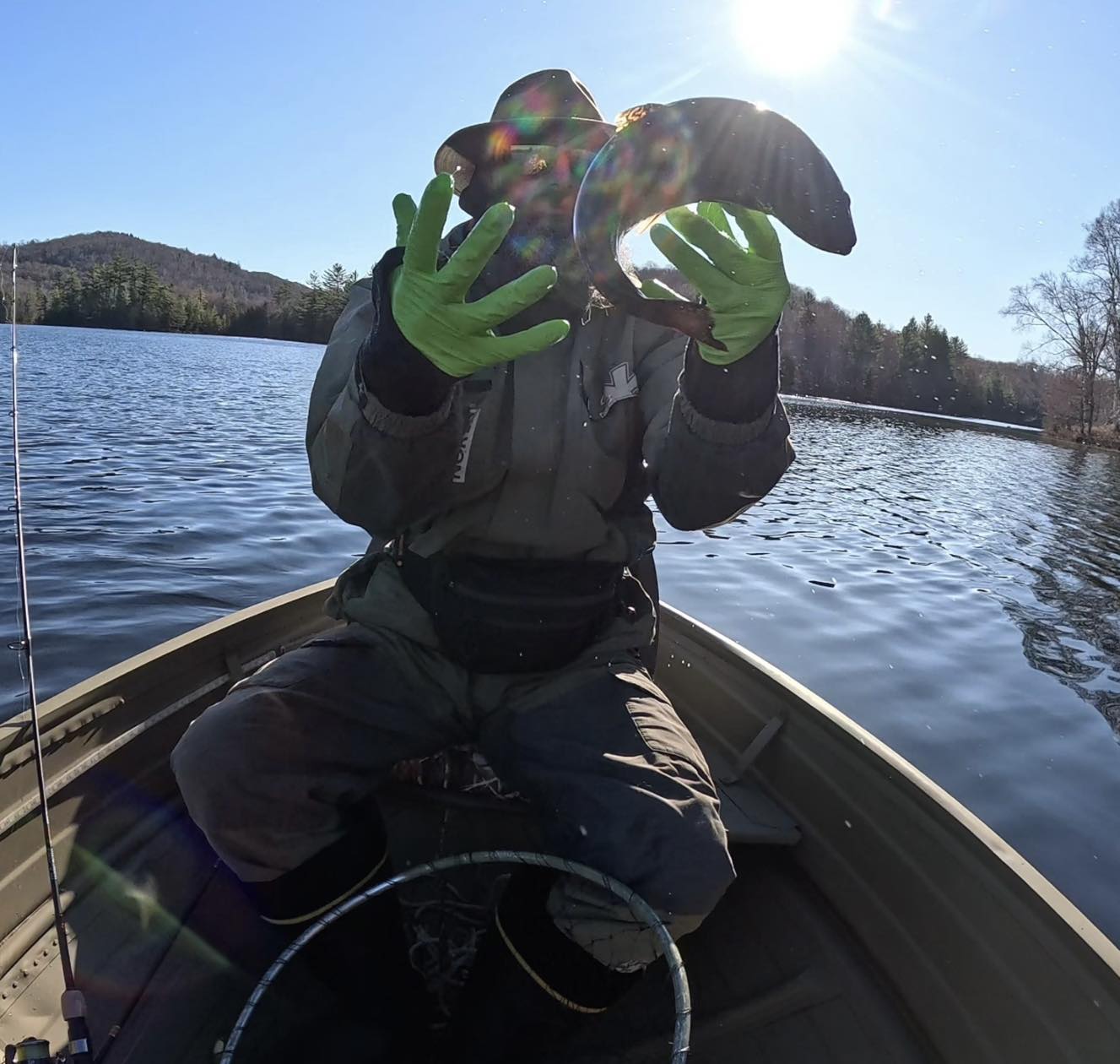Angler in boat on lake using binoculars to spot fish in Paul Smiths NY
