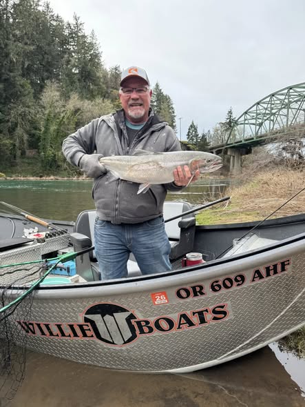 Angler holding large fish catch standing in drift boat on river in Myrtle Creek OR