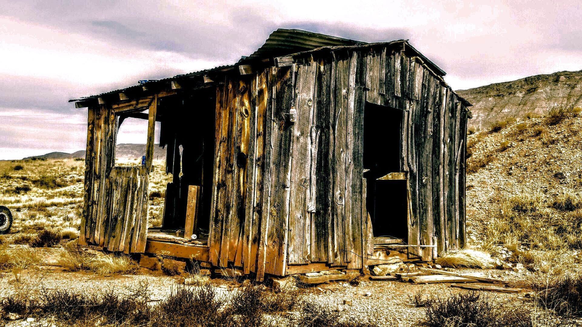 Weathered wooden cabin in desert landscape with corrugated metal roof and open doorway