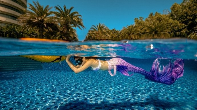 Person learning mermaid swimming technique underwater with colorful tail fin in clear blue water