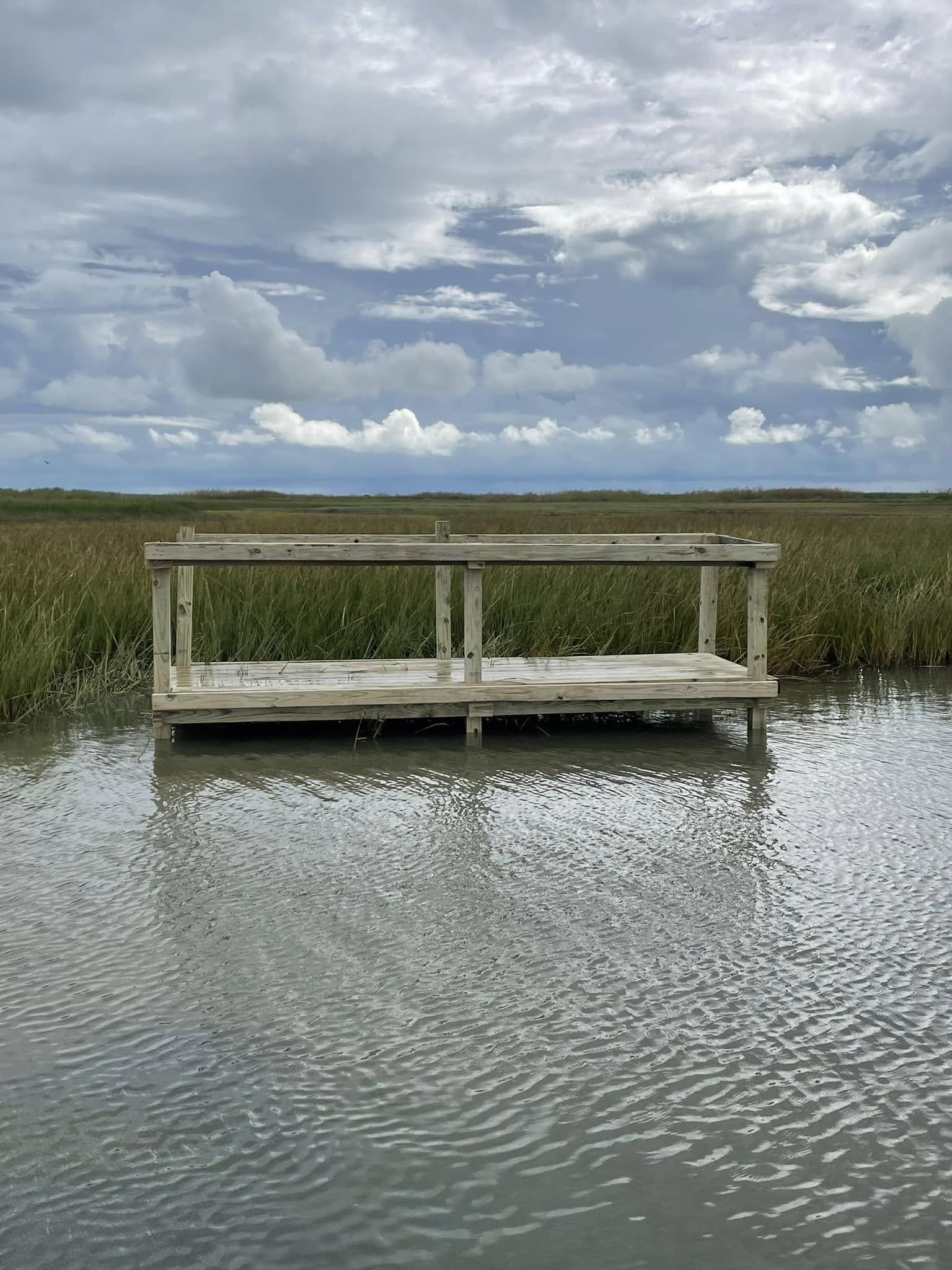 Wooden fishing dock extending over shallow water with marsh grass in Port O'Connor TX