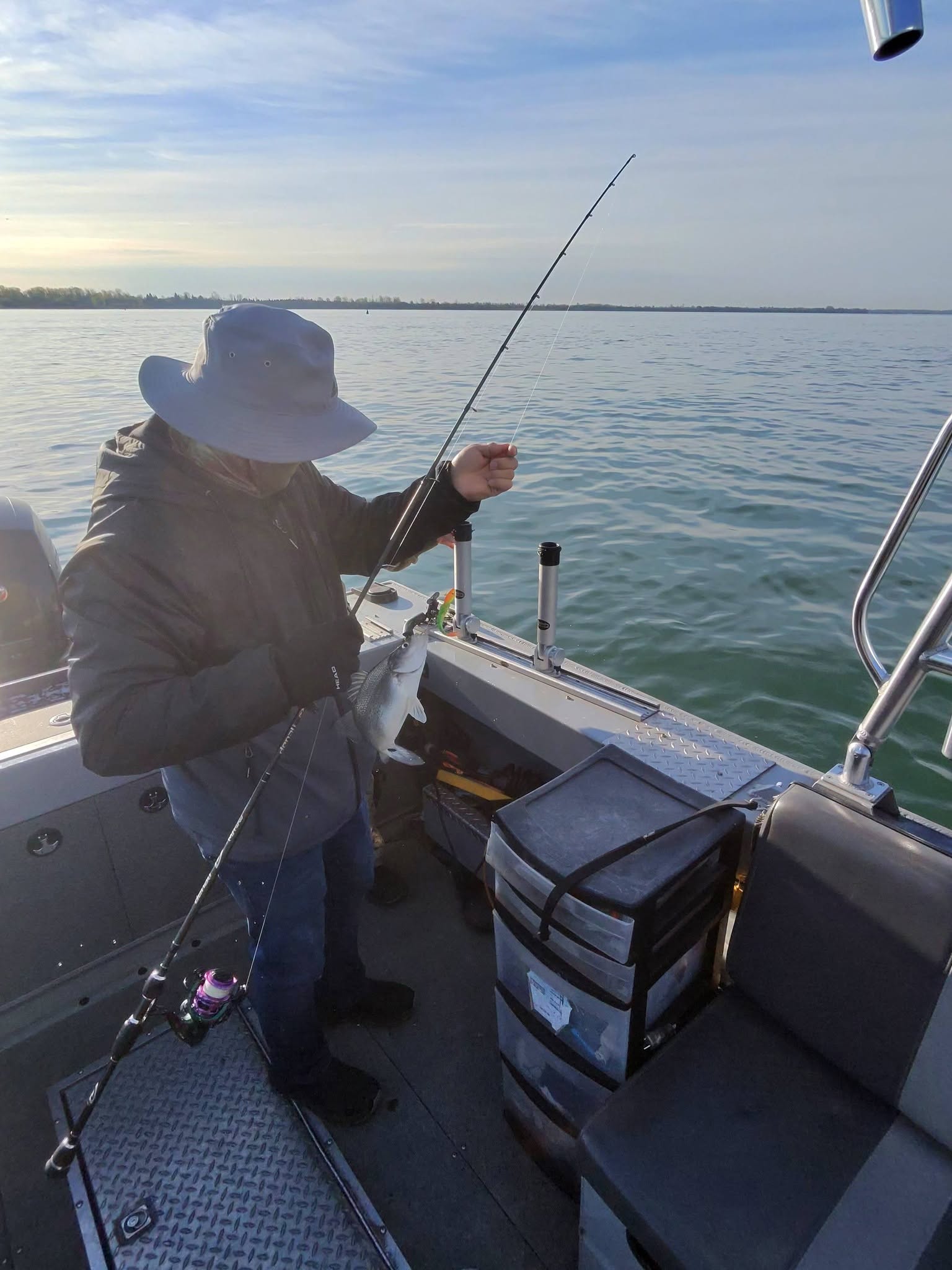 Fishing from boat on calm water in Detroit MI with fishing rod and tackle boxes