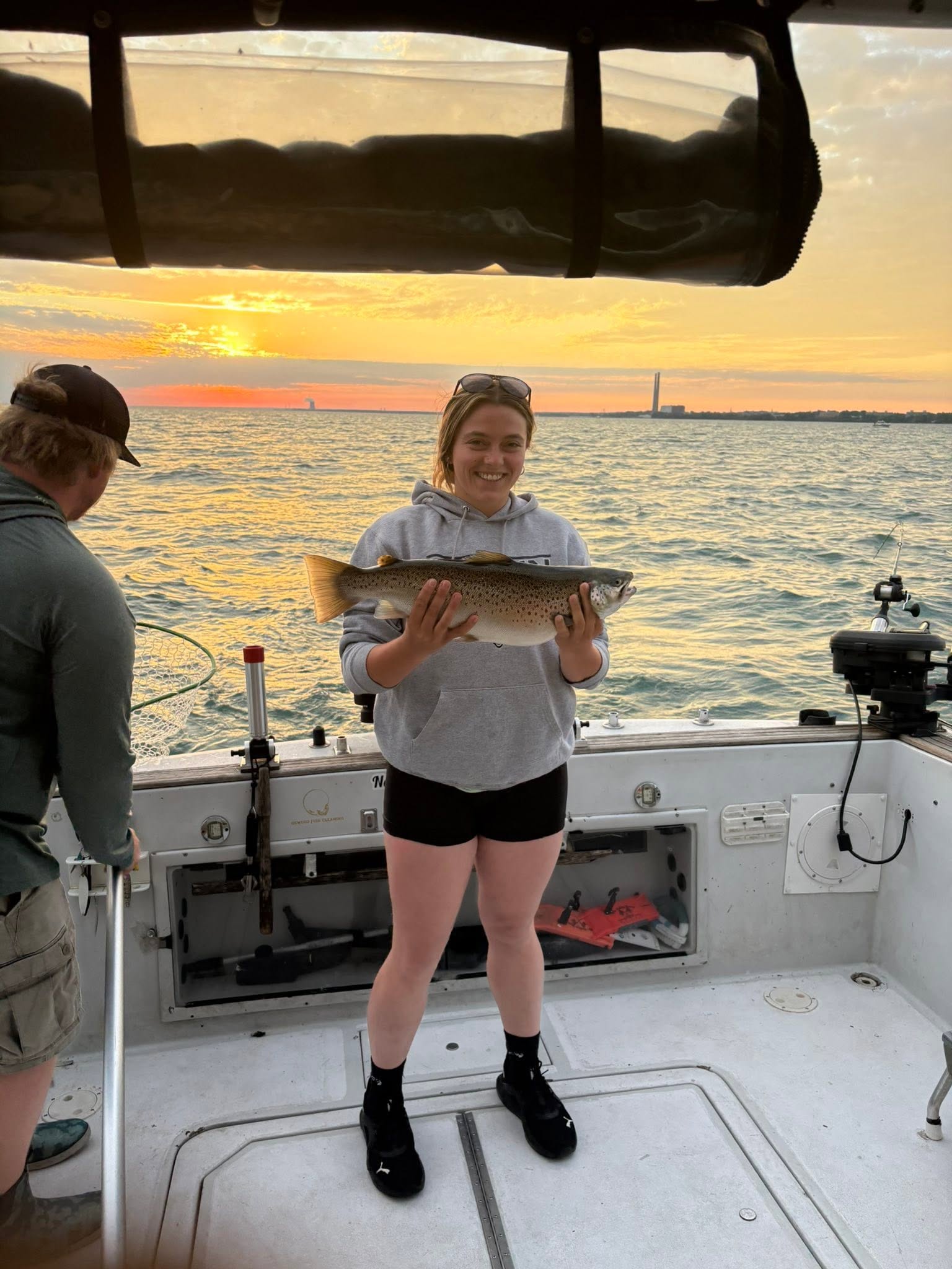 Angler holding caught fish on boat deck during sunset fishing trip in Oswego NY