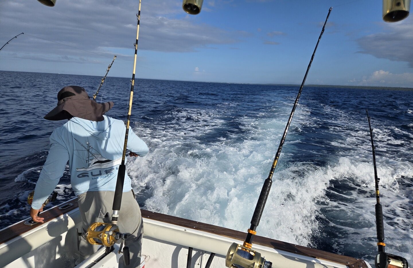 Deep sea fishing boat trolling with multiple fishing rods in blue ocean waters near Dominicus