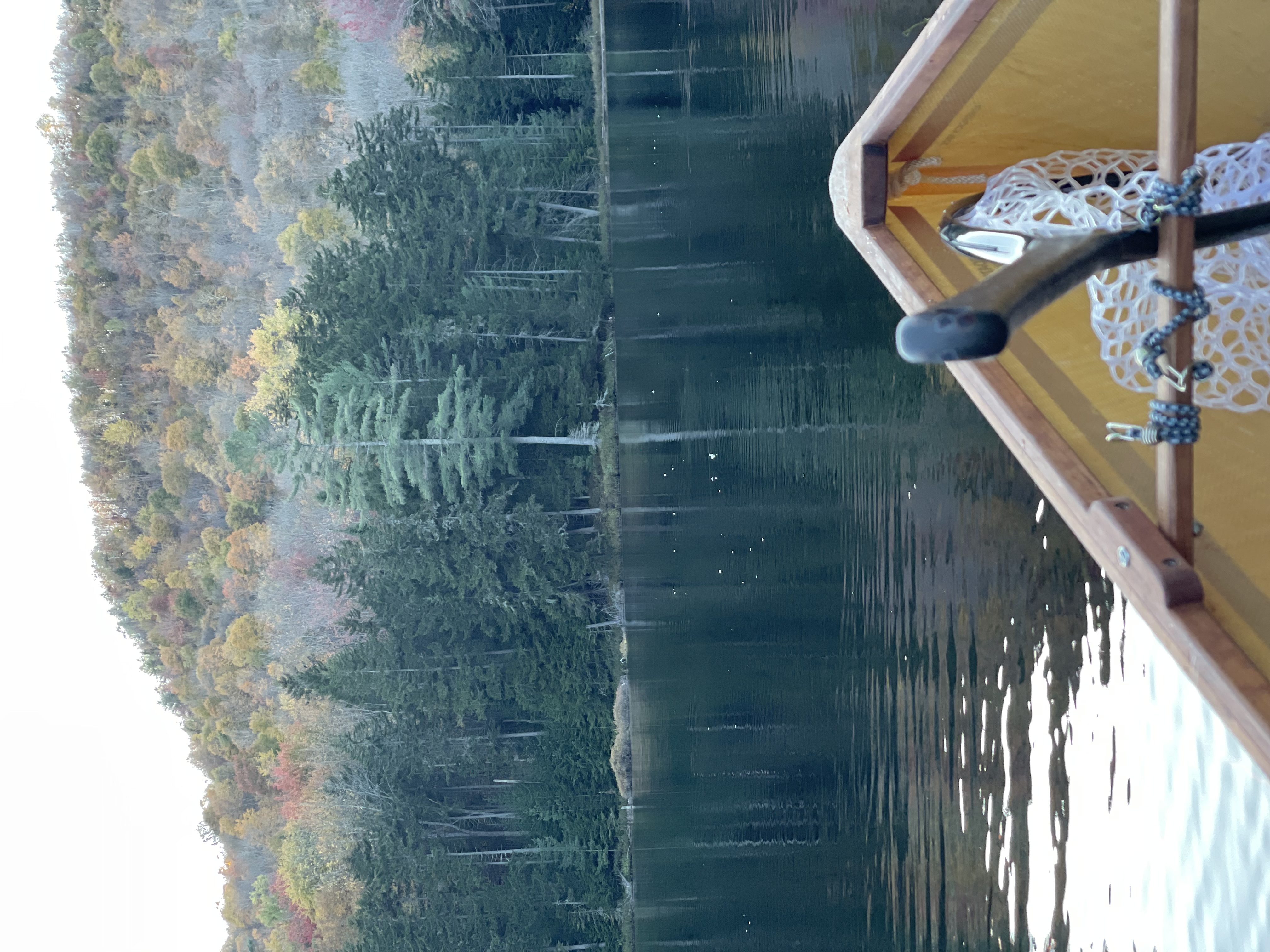 Fishing scene on Saranac River New York with boat near forested shoreline in autumn