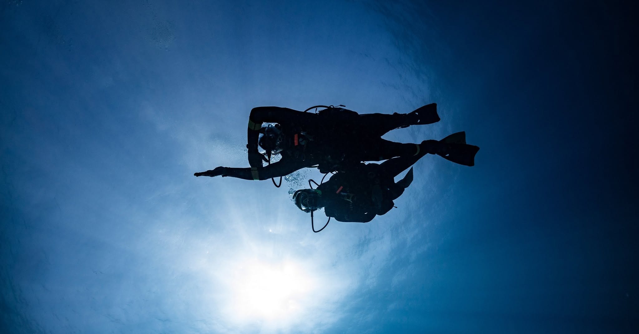 Underwater view of scuba diver silhouetted against bright sunlight filtering through water
