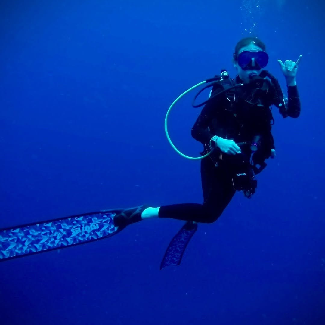 Scuba diver underwater in deep blue ocean water making hand gesture