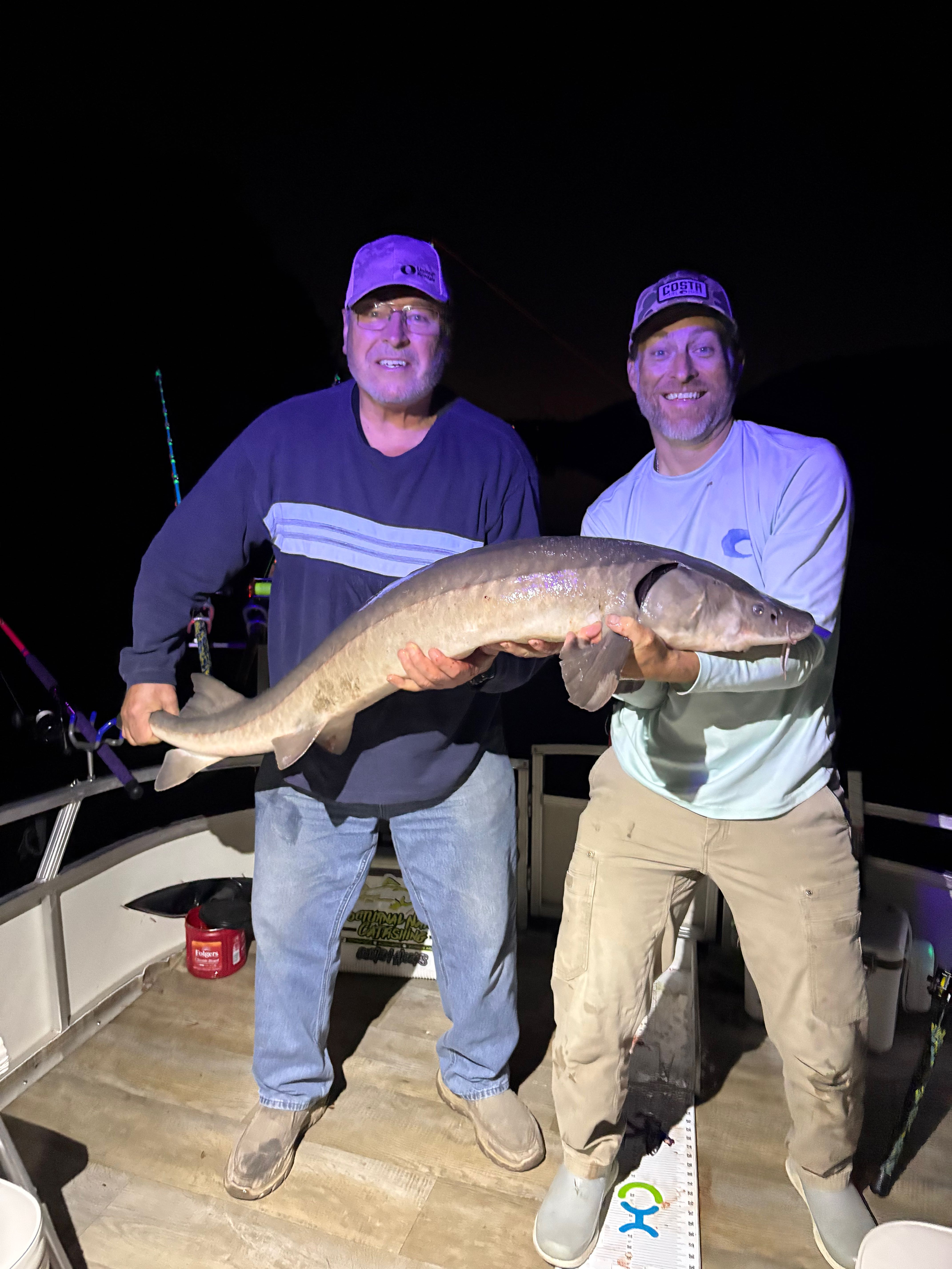 Two anglers holding large Lake Sturgeon catch on fishing boat in Stillwater MN