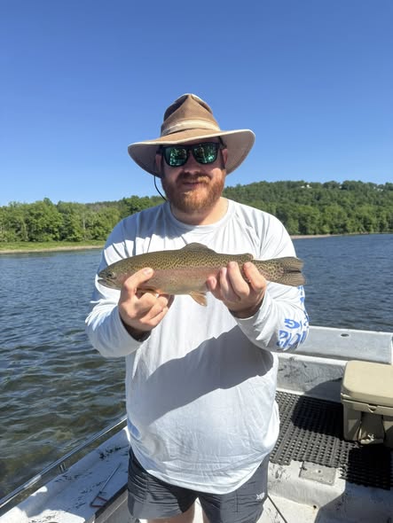 Rainbow trout caught fishing in Cotter AR on boat with forested shoreline