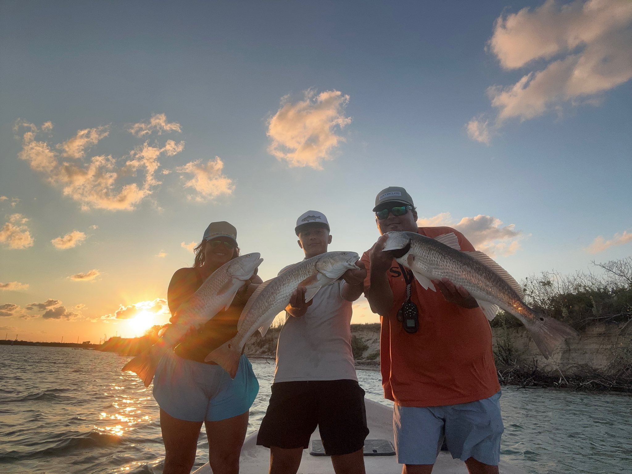 Three anglers displaying caught redfish during sunset fishing trip in Rockport TX