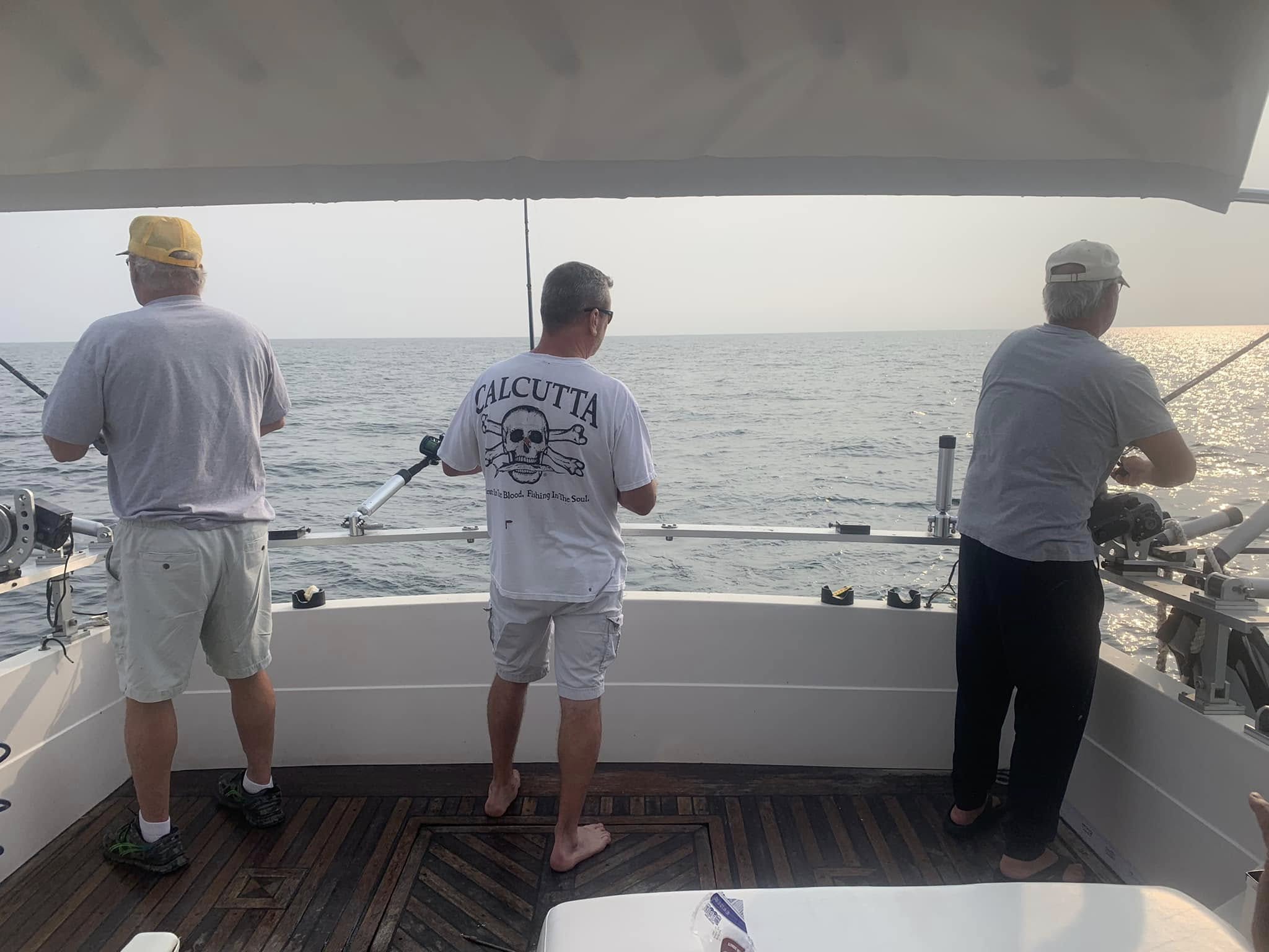 Three anglers fishing from the stern of a fishing boat on open water in Burt NY