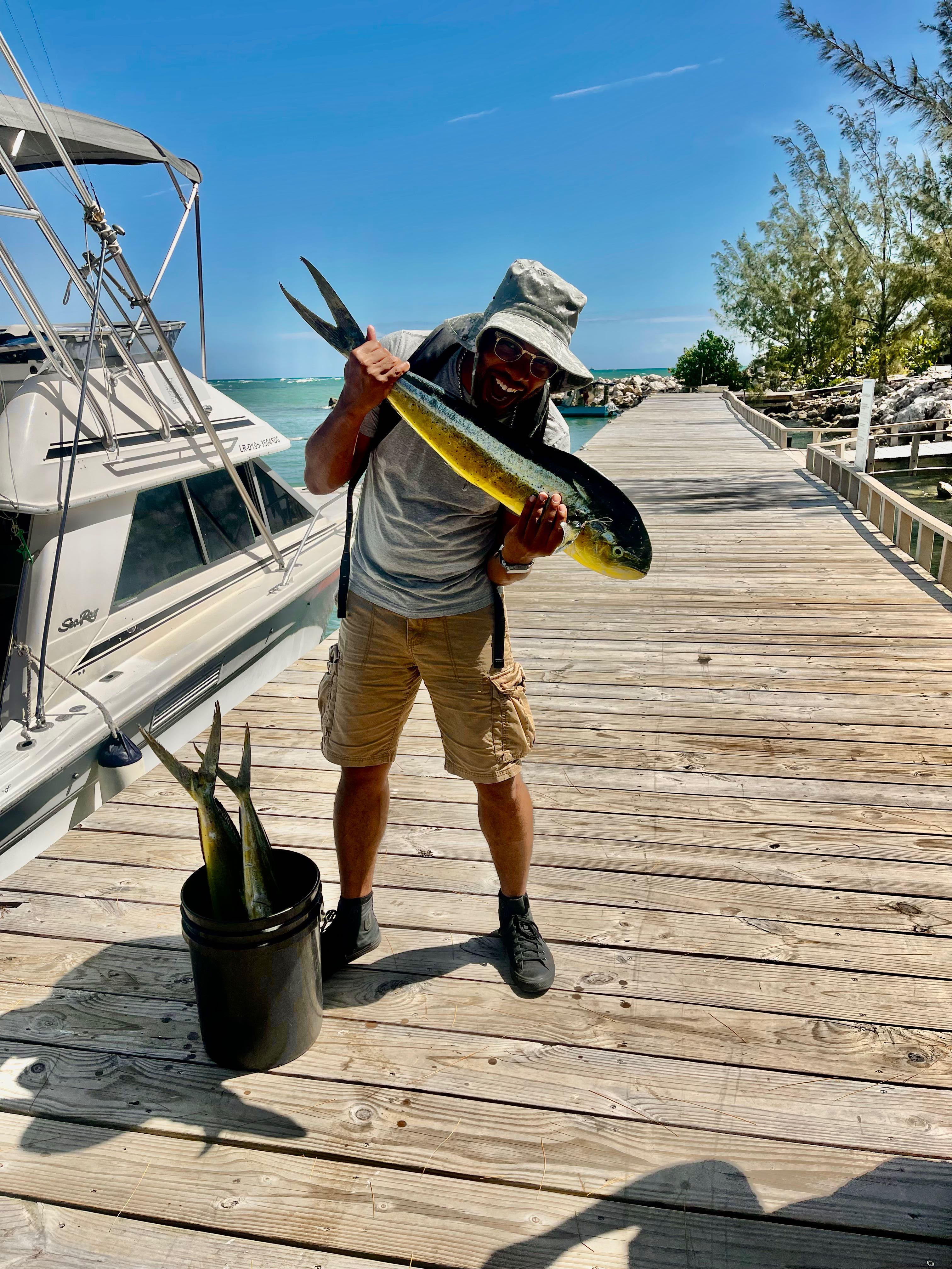 Fresh caught mahi mahi fish displayed on wooden dock in Puerto Plata with fishing boat nearby