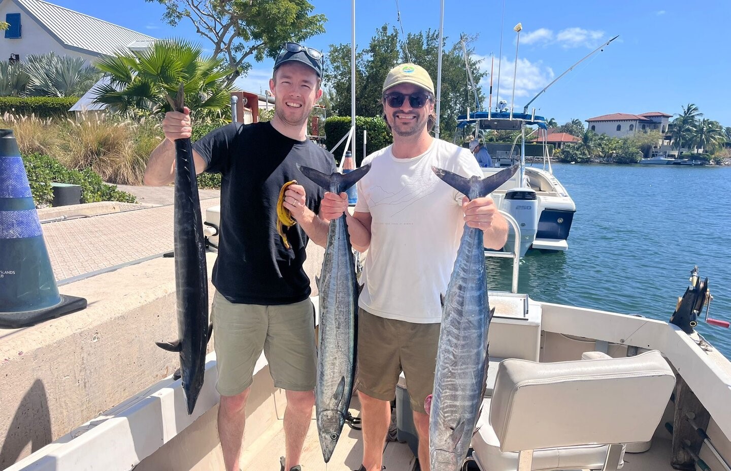 Two anglers displaying freshly caught wahoo fish on dock at West Bay marina with boats in background