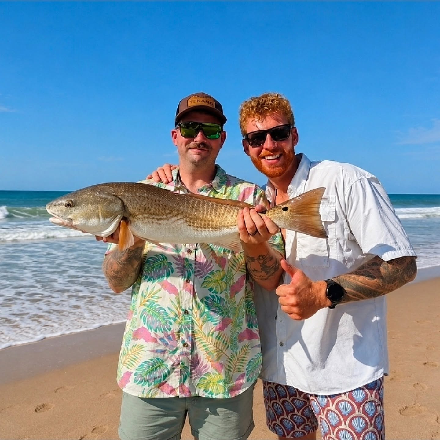 Two anglers holding a redfish on Mount Pleasant SC beach with ocean waves in background