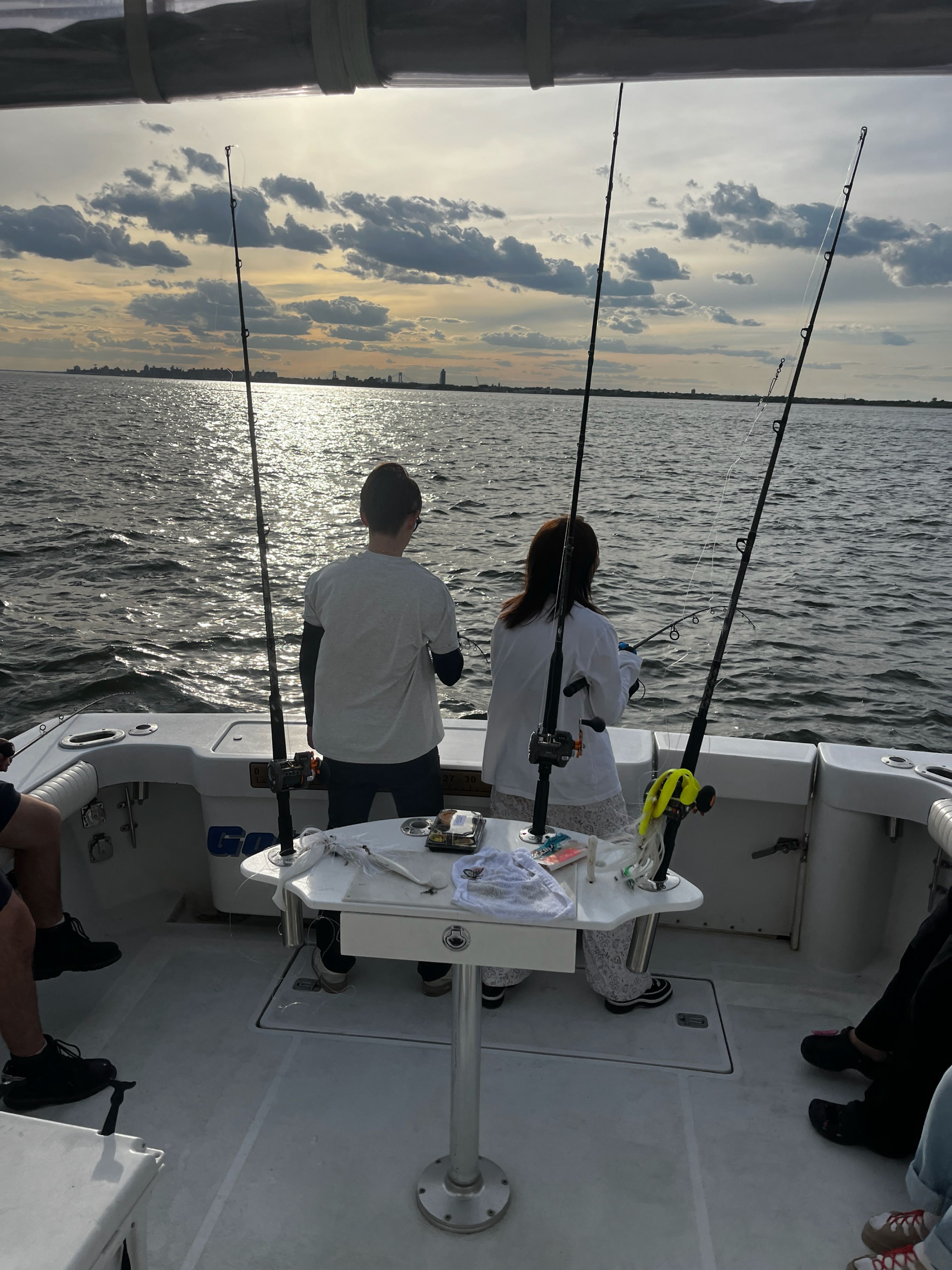 Fishing boat with multiple rods set up on open water near New York City coastline during evening hours