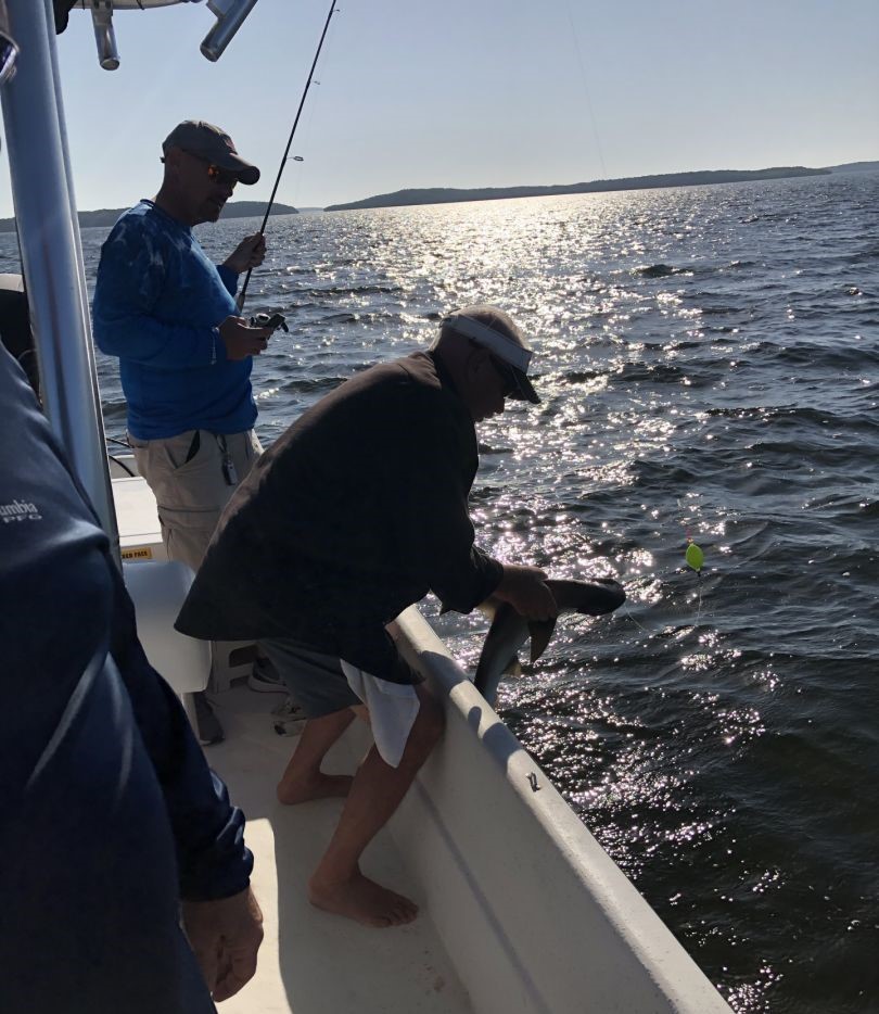 Fishing boat on sparkling water in Crystal River FL with angler holding rod and person leaning over gunwale