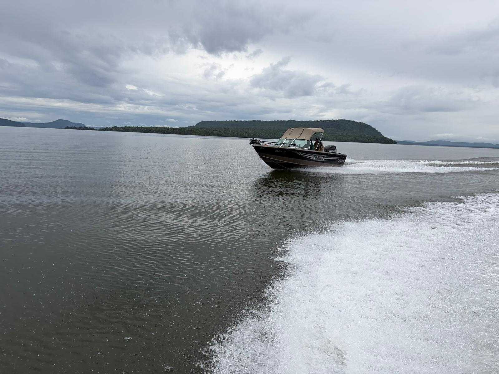 Fishing boat speeding across water near forested shoreline in Nipigon ON