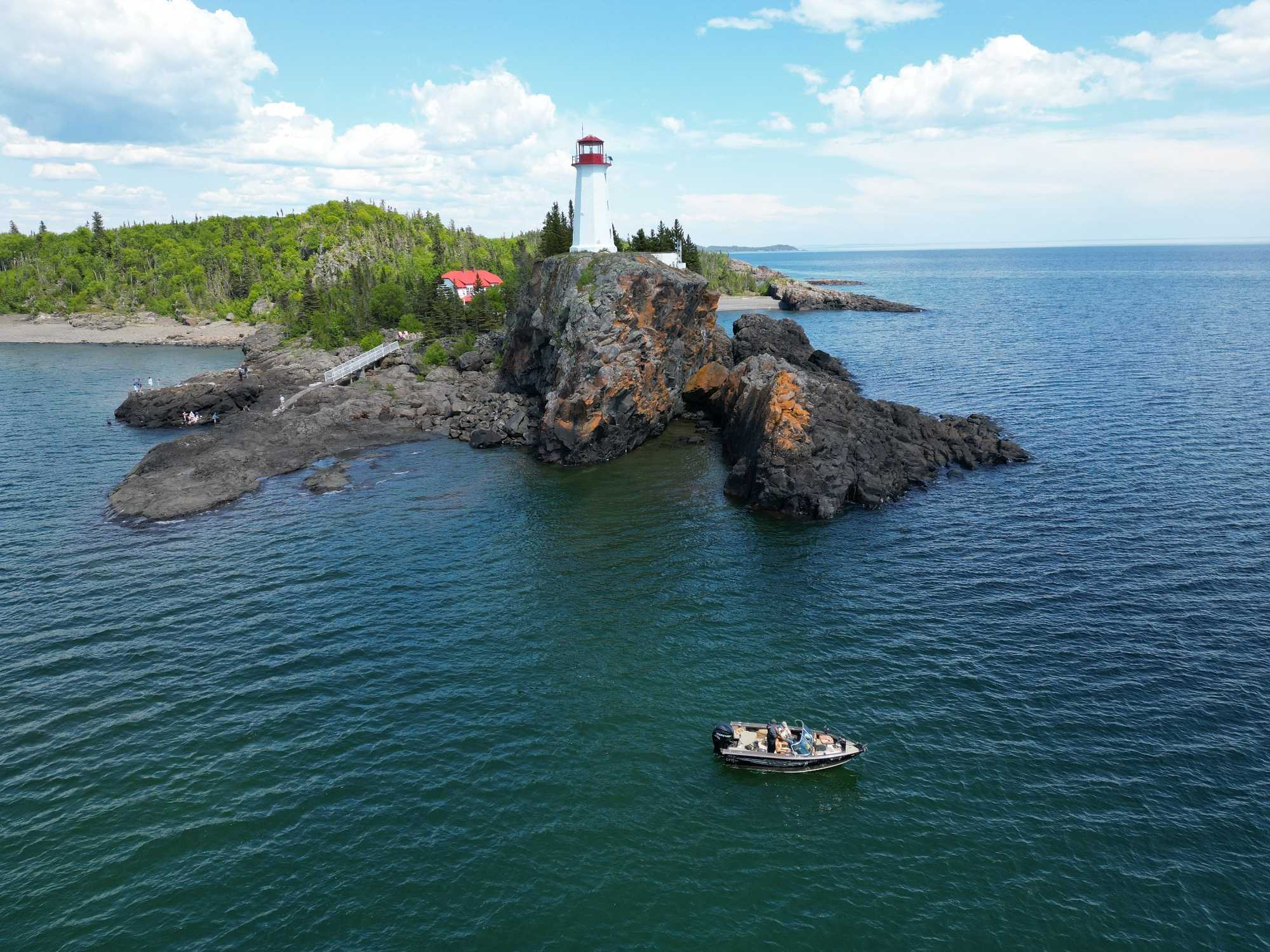 White lighthouse on rocky island with fishing boat in turquoise waters near Nipigon ON