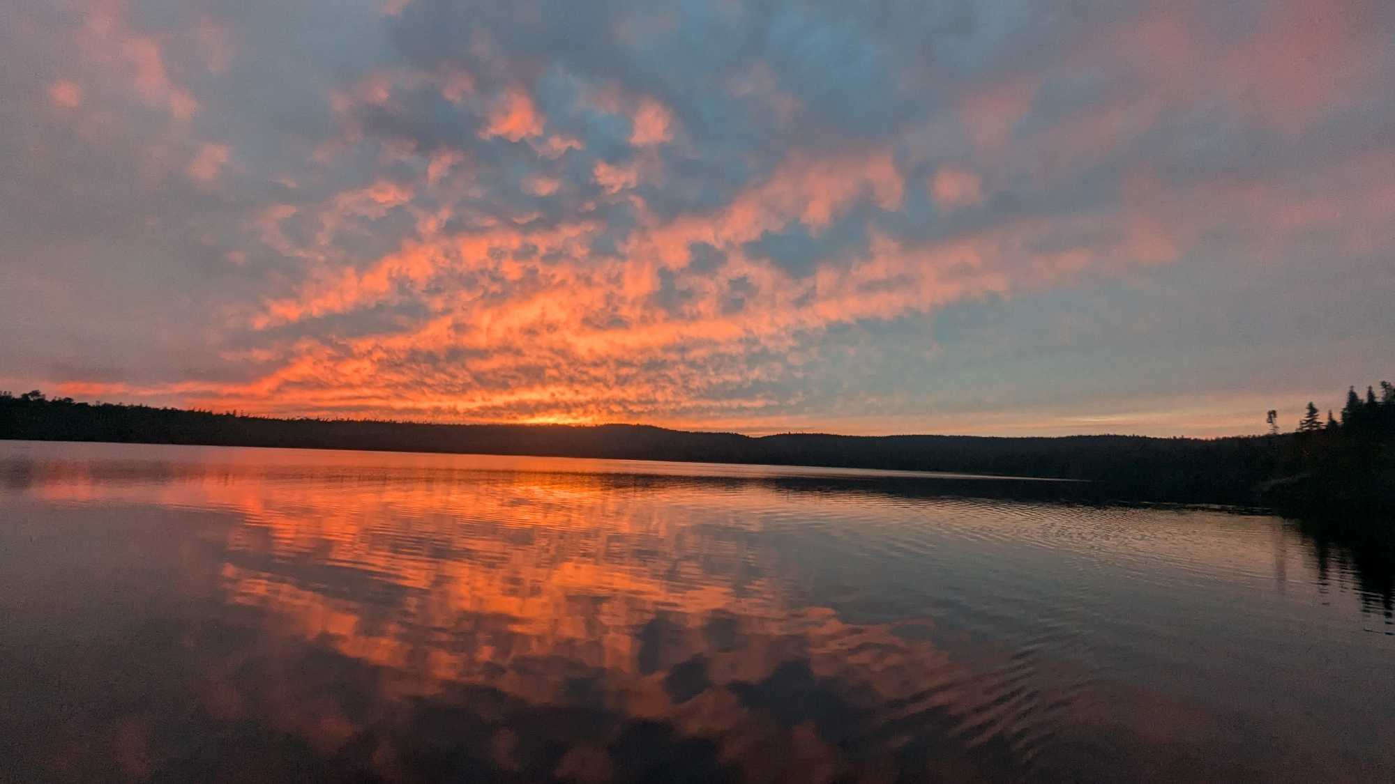 Dramatic sunset sky with orange and pink clouds reflecting on calm lake waters in Nipigon ON