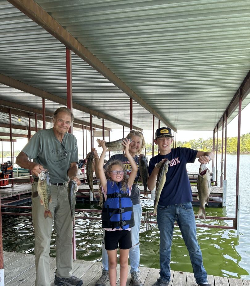 Four people displaying freshly caught bass on a covered boat dock in Branson MO