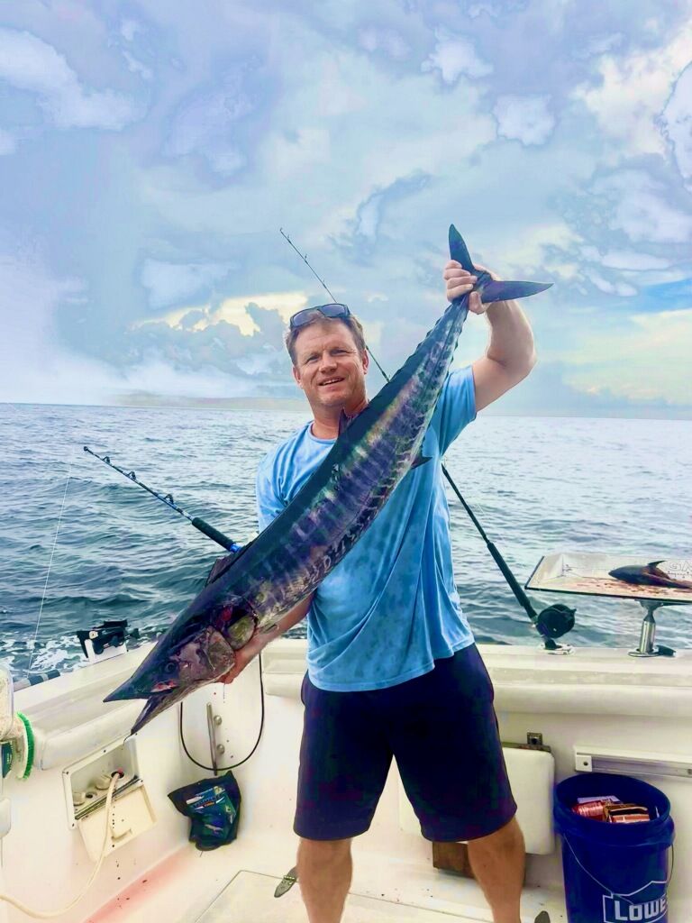Angler holding large wahoo fish on fishing boat deck with ocean background