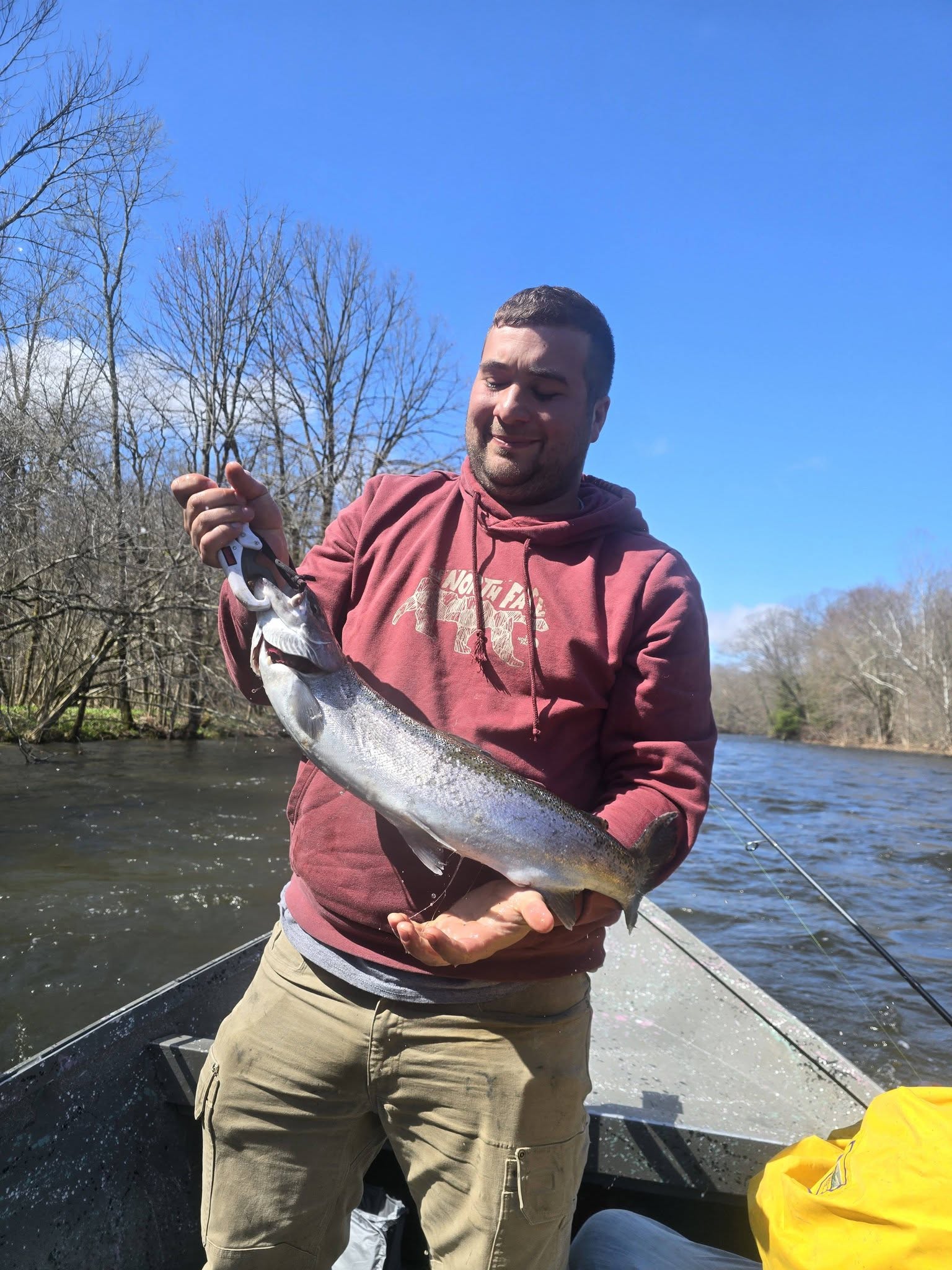 Angler holding caught salmon on boat in Altmar NY river