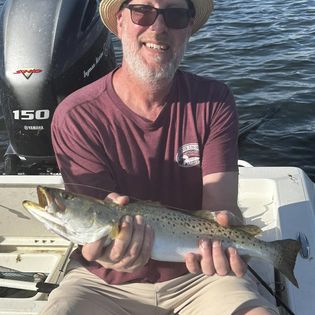 An angler holds a fish in front of a coastal location in Fort Myers.
