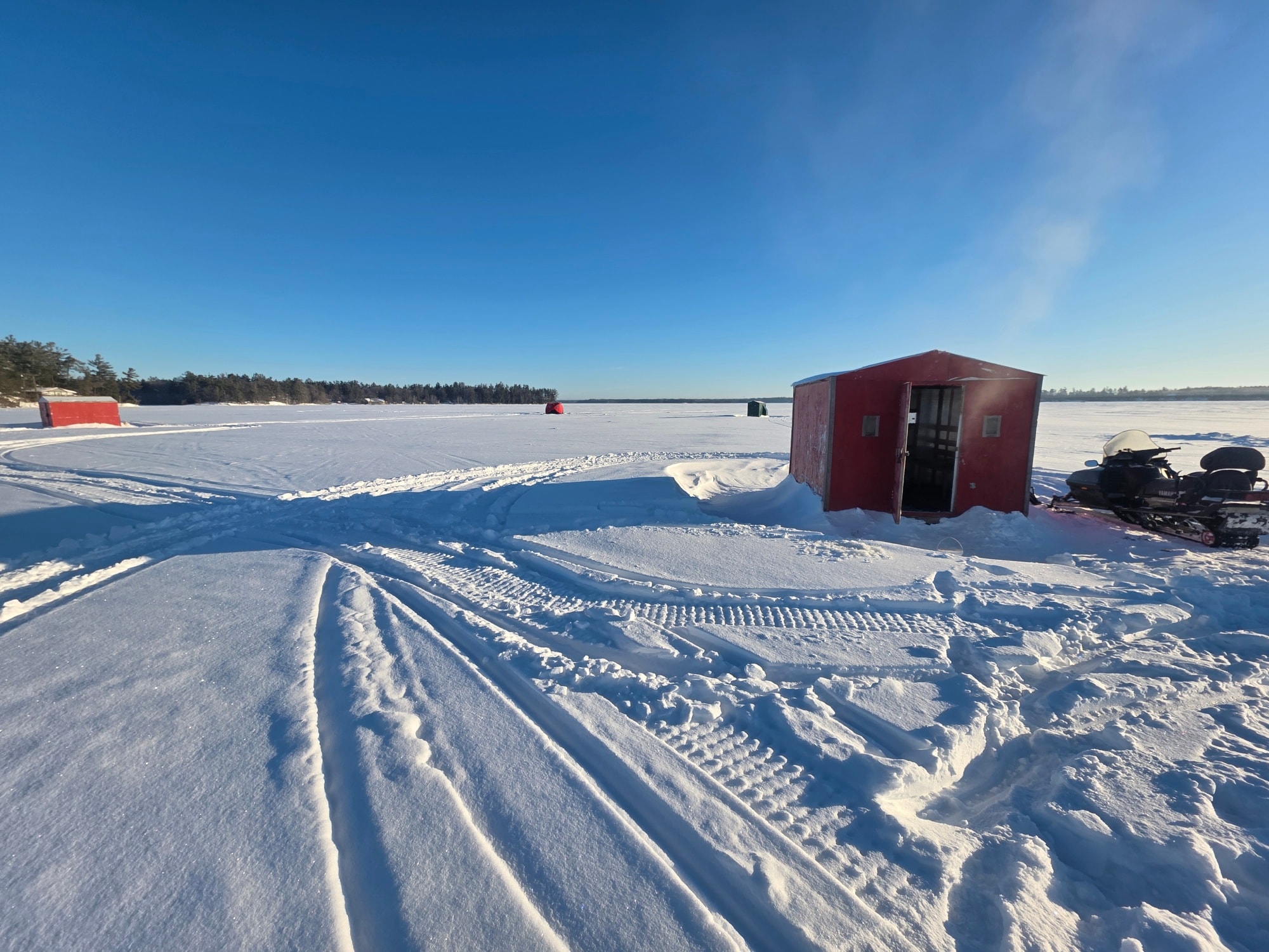 Ice fishing setup on frozen lake in Gravenhurst ON with red shelter and snowmobile tracks
