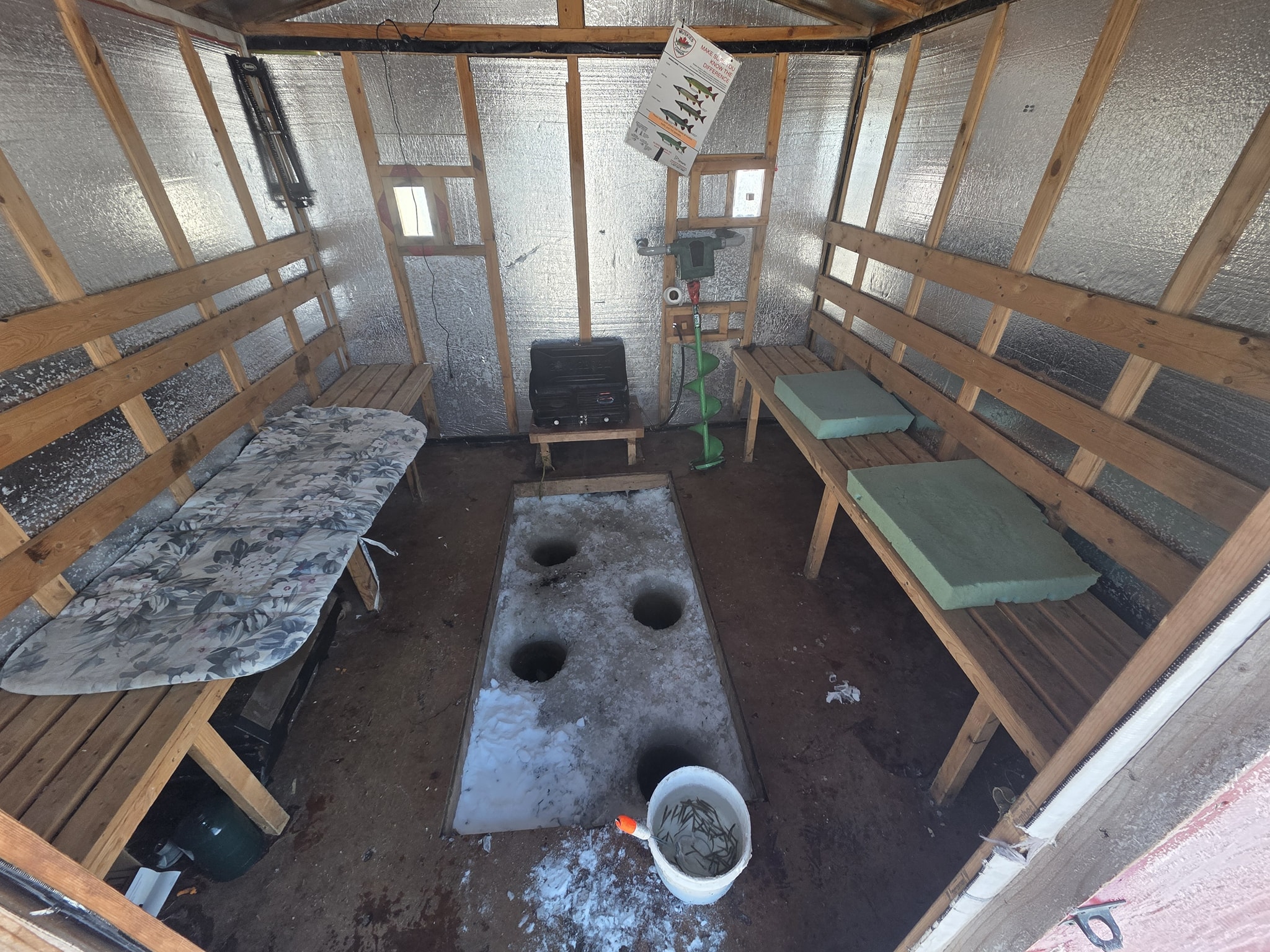 Ice fishing hut interior in Gravenhurst ON with wooden benches, holes cut in ice floor, and fishing equipment