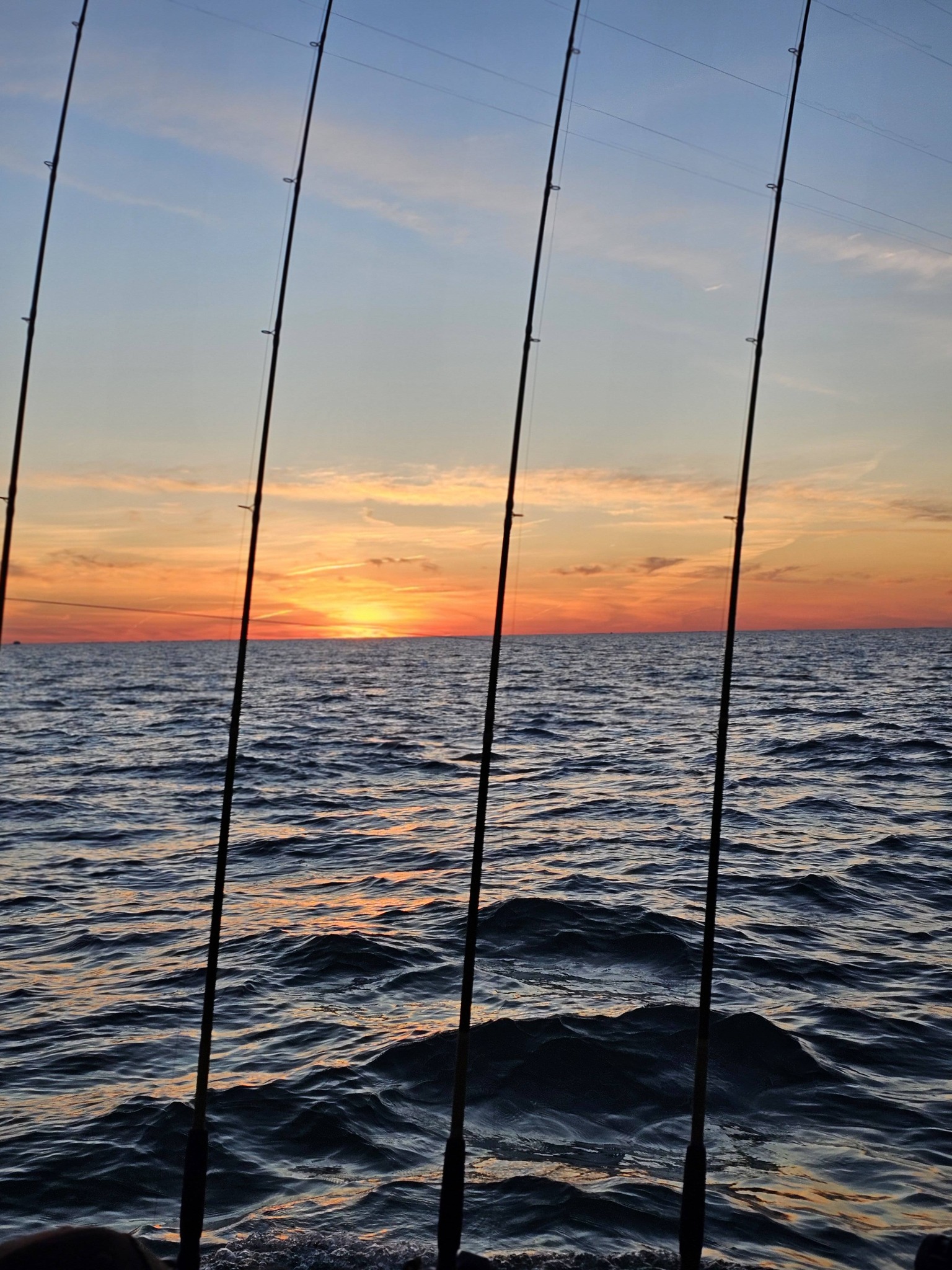 Fishing rods silhouetted against sunset over choppy waters in Port Clinton OH