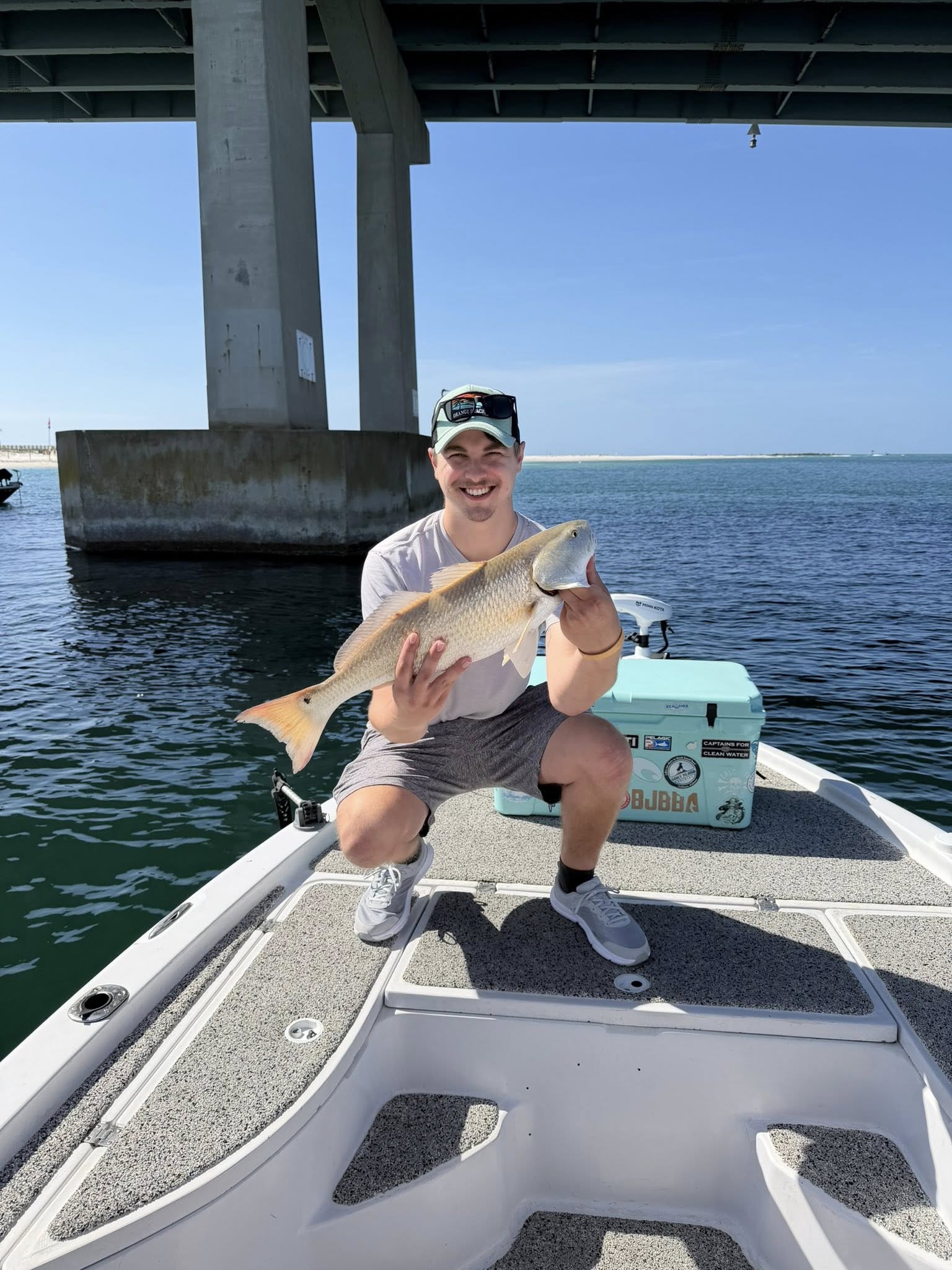 Angler holding caught redfish on fishing boat near bridge in Orange Beach Alabama