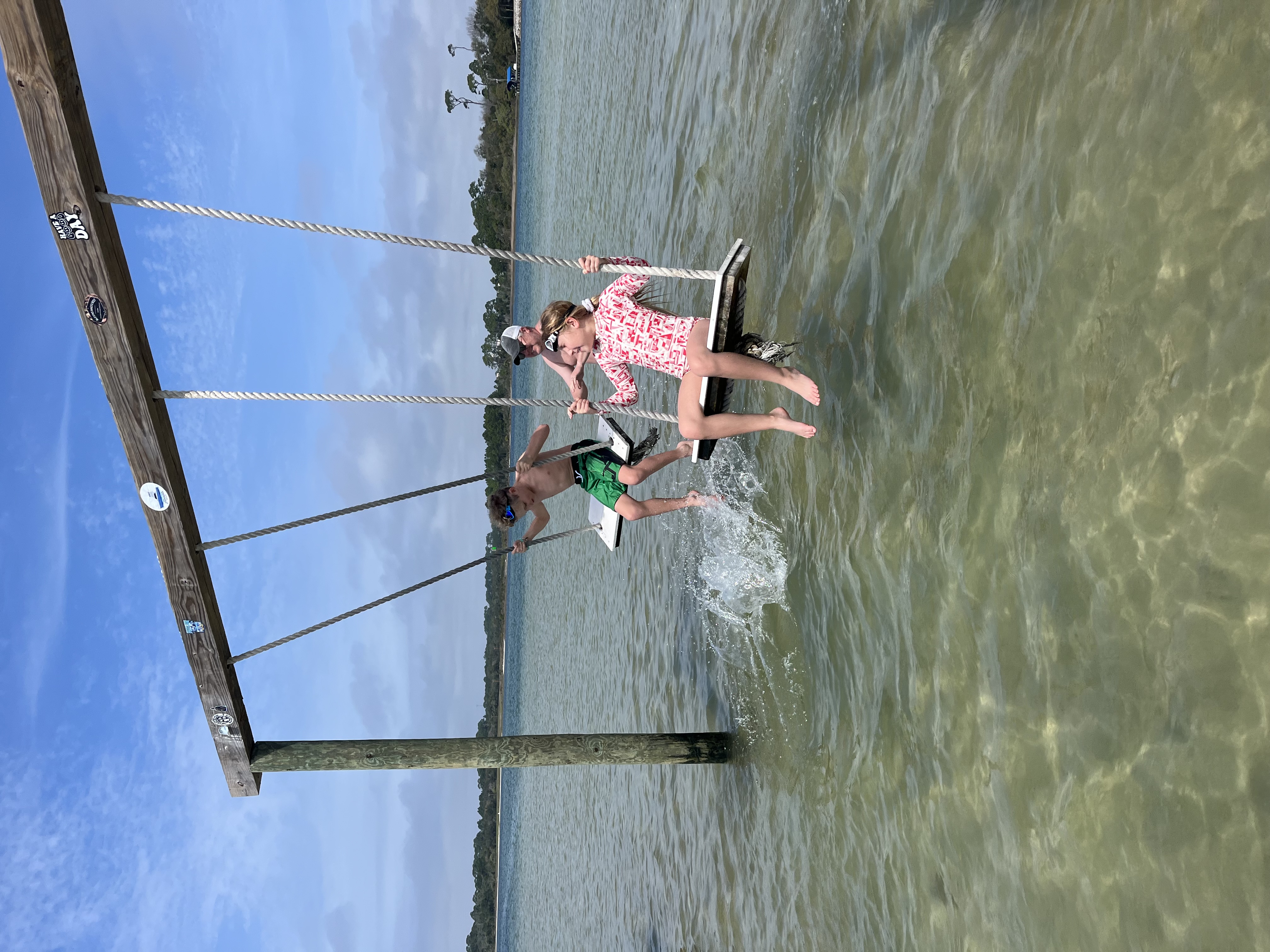 Two people jumping from rope swing into clear water during cruise excursion