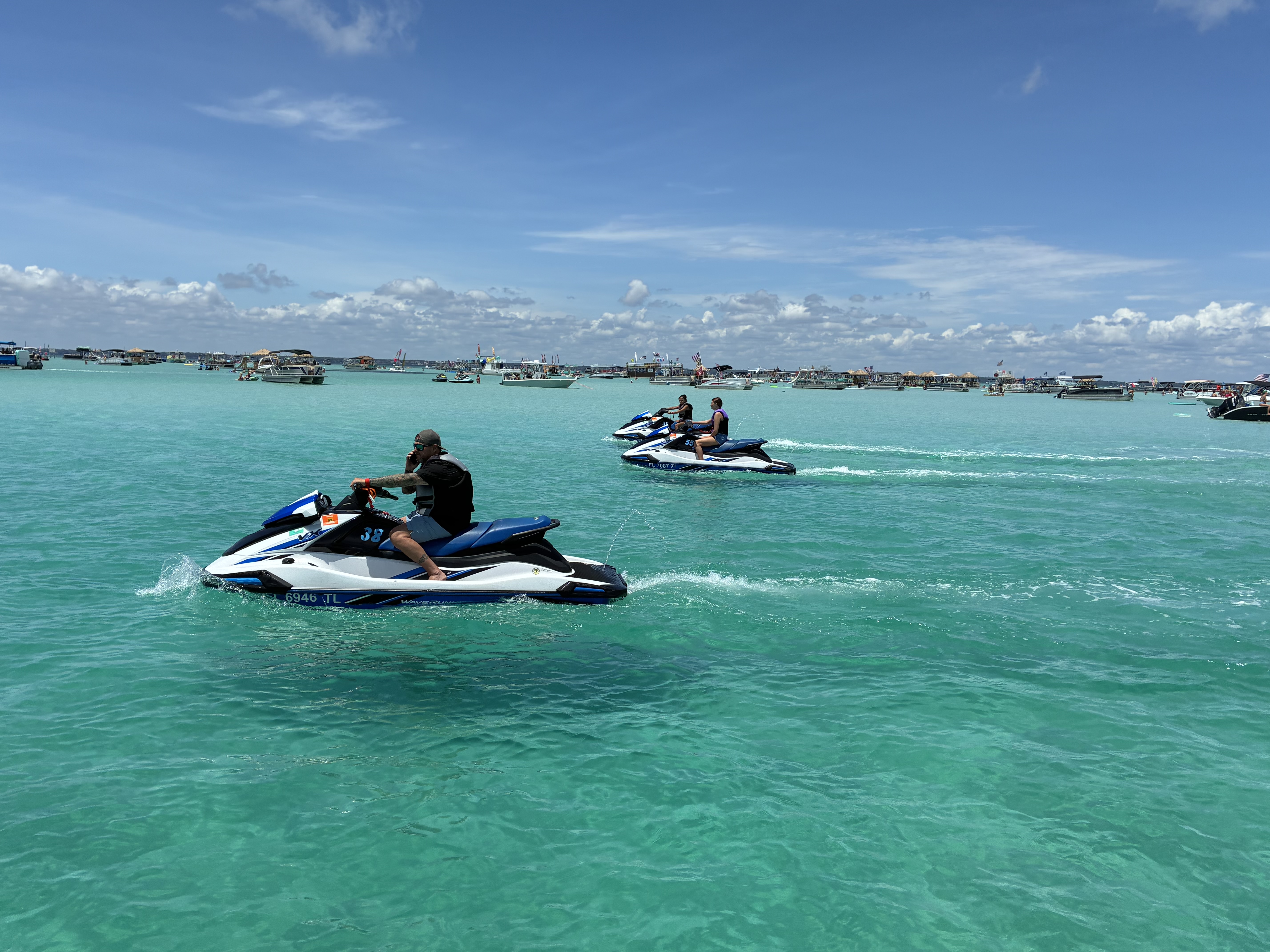 Two jet skis racing across crystal clear turquoise water with boats anchored in the background