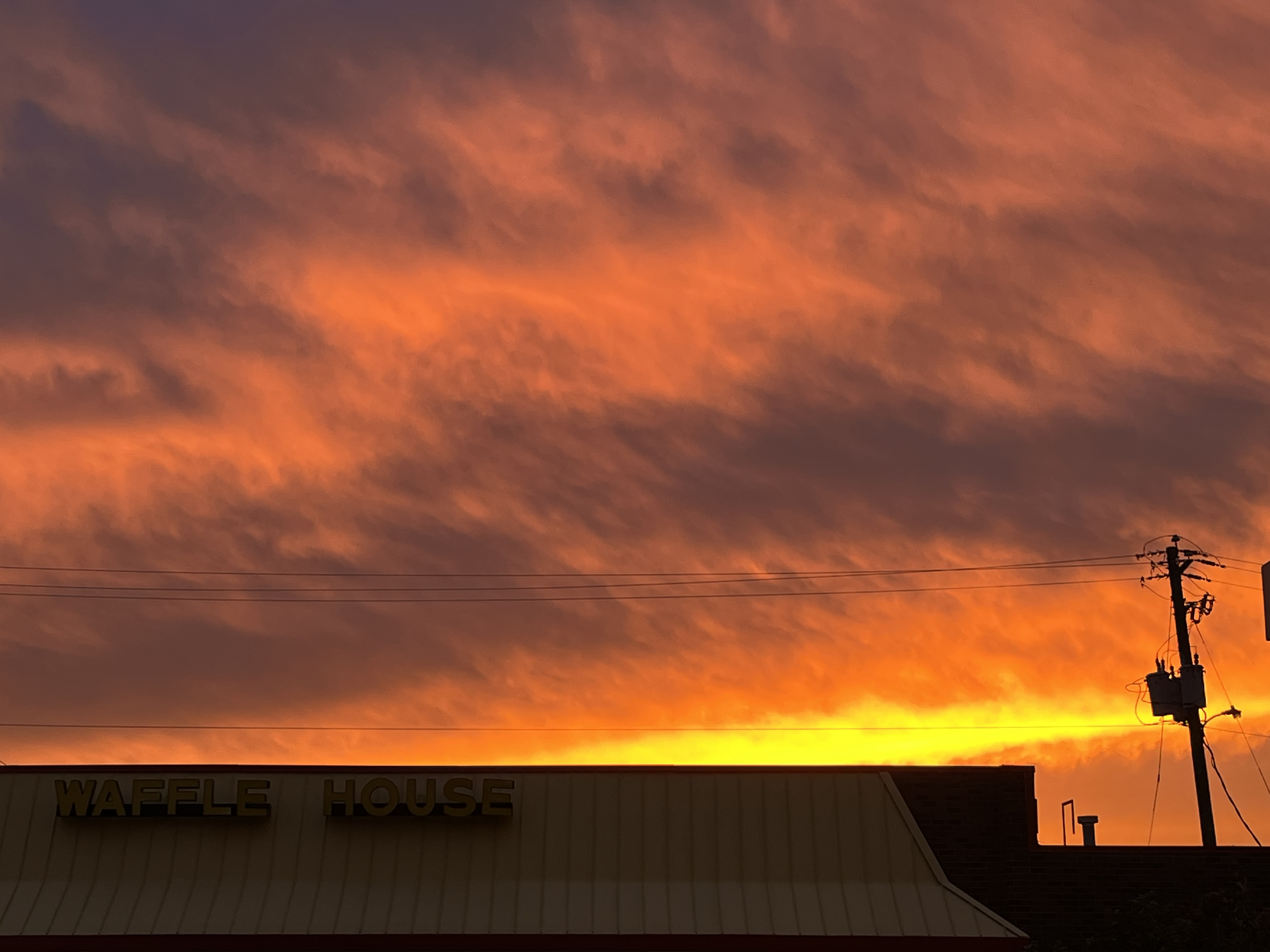 Dramatic orange and red sunset sky with clouds over Waffle House restaurant building and power lines