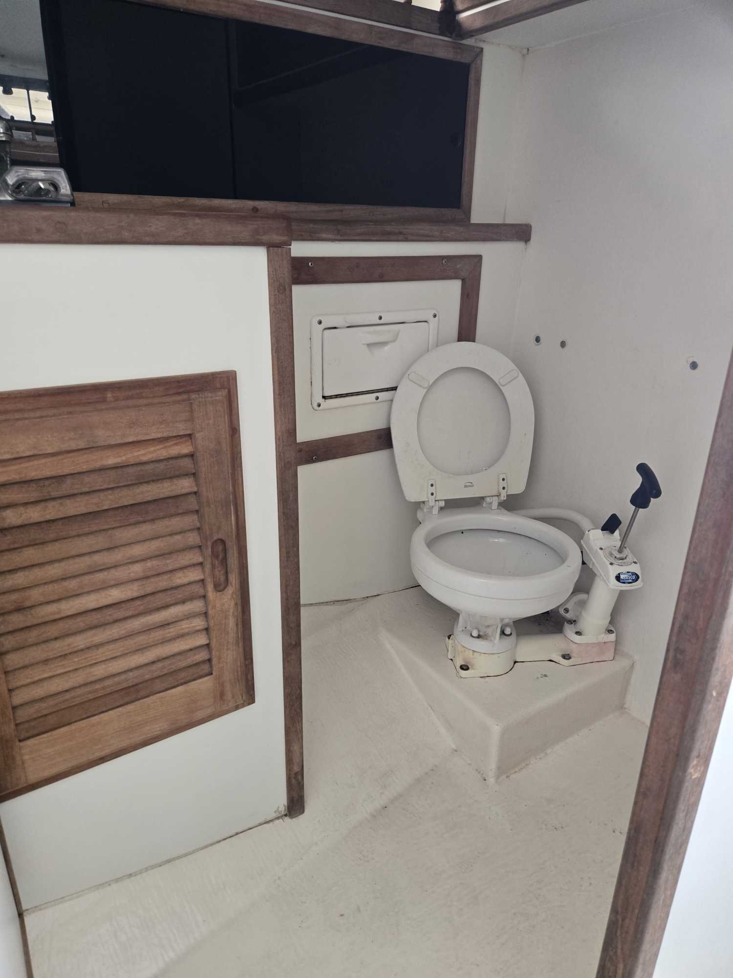 Marine toilet in boat head compartment with wooden cabinetry and access panel on Cape Cod