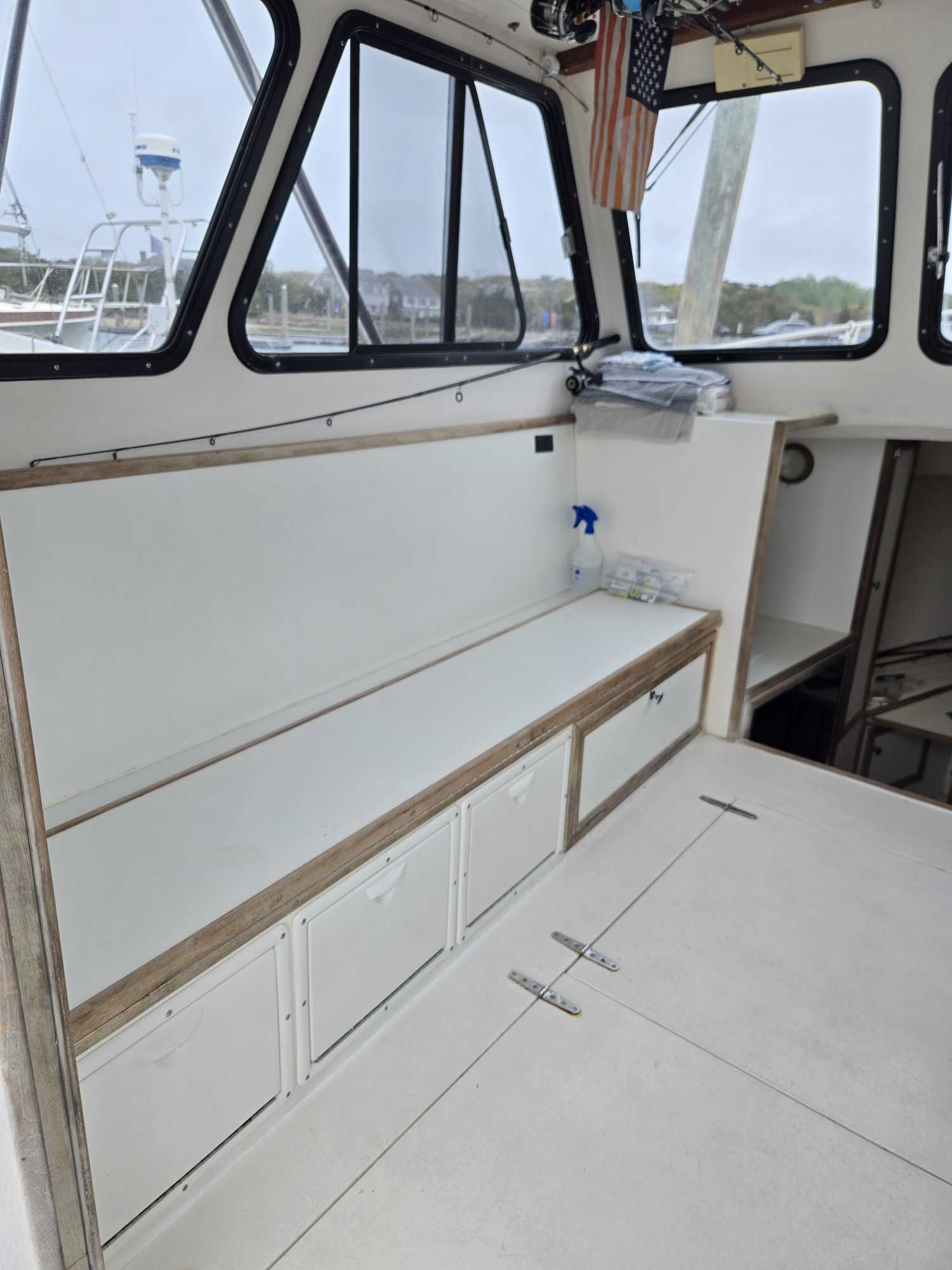 Interior of fishing boat cabin with white built-in seating and storage, windows overlooking Cape Cod MA marina