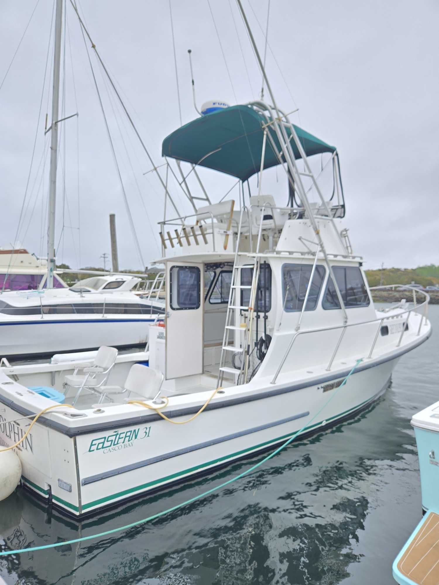 White fishing boat named Eastean 31 docked at Cape Cod MA marina with green canvas top and fishing equipment