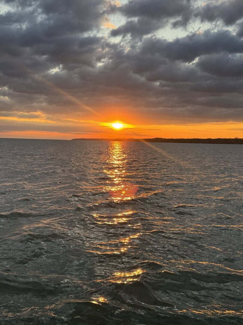 Sunset over water with golden light reflection creating wake pattern on surface in Erie PA