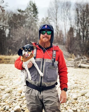 Fishing guide holding dog on rocky riverbank in Willow Alaska