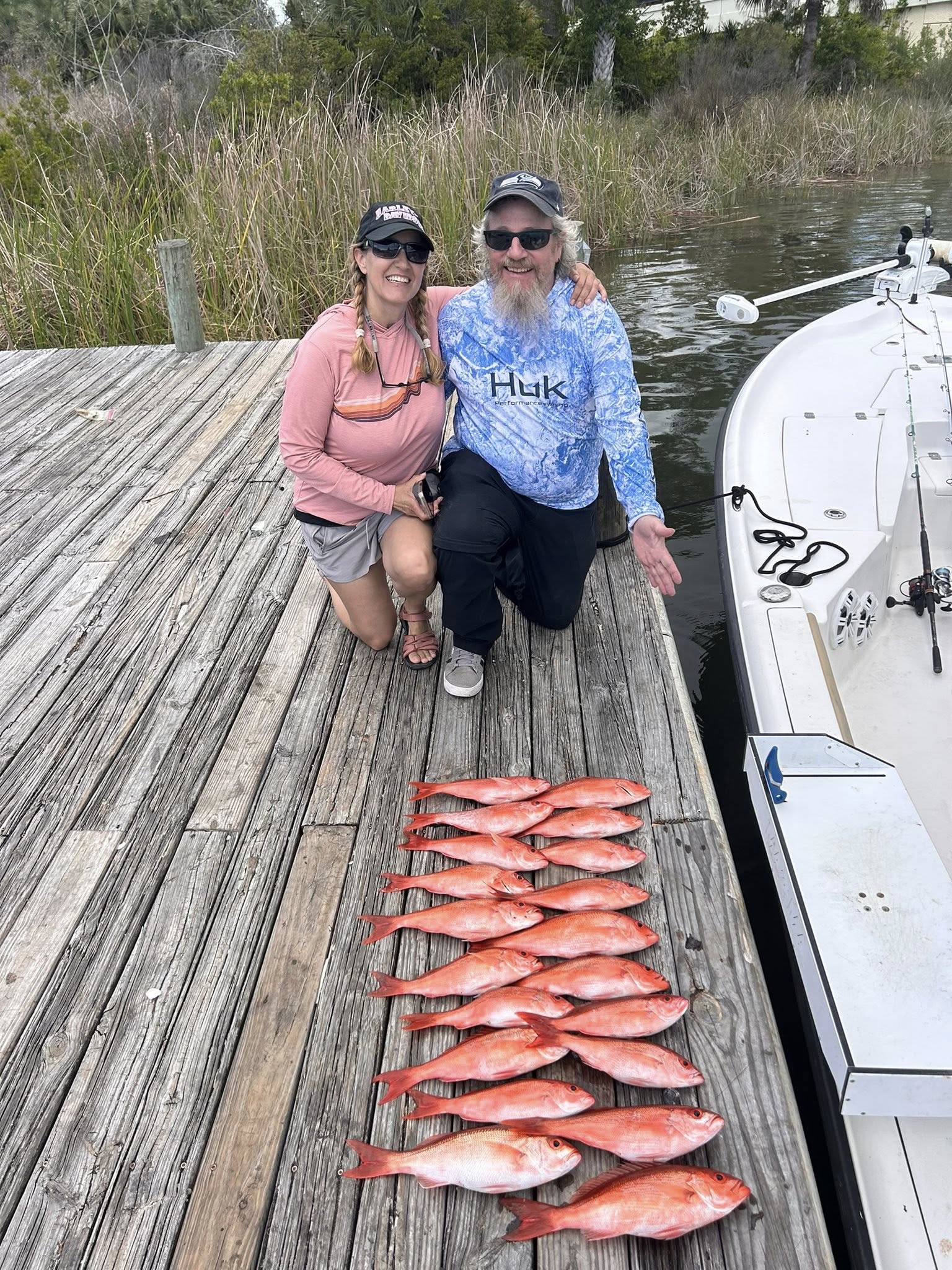 Successful fishing trip in Pensacola FL showing caught red snapper laid out on wooden dock with boat nearby