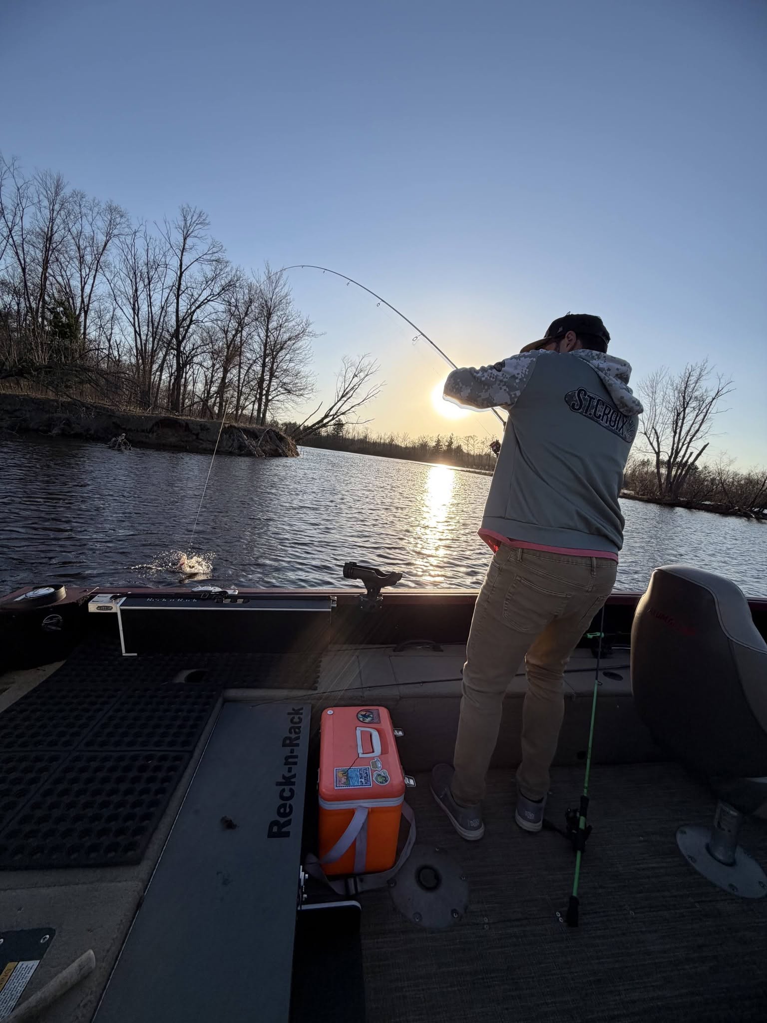 Angler fishing from boat at sunset on lake in Mosinee Wisconsin with bent fishing rod indicating active catch