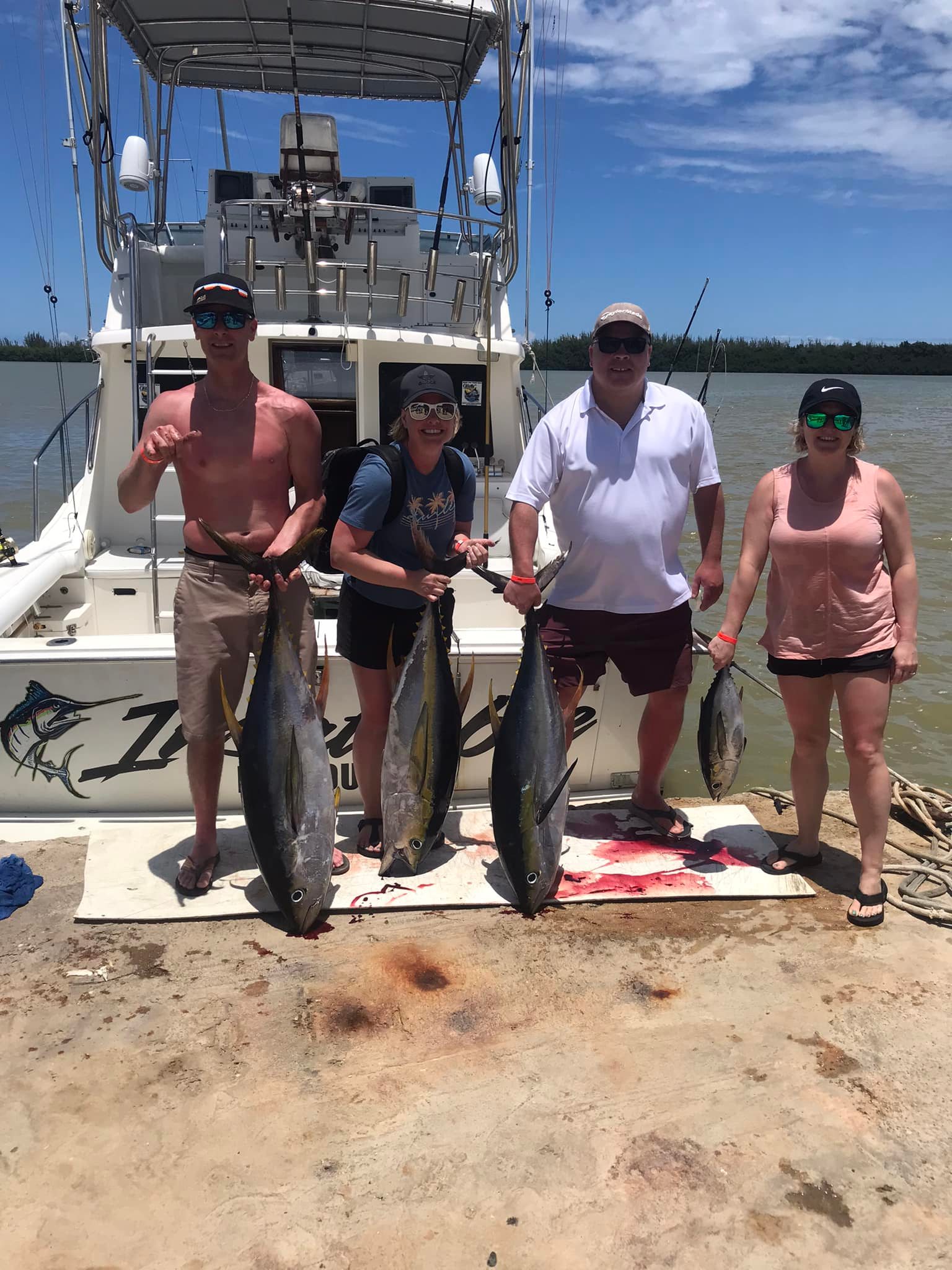 Four large tuna fish displayed on dock after successful fishing trip in Falmouth with charter boat in background