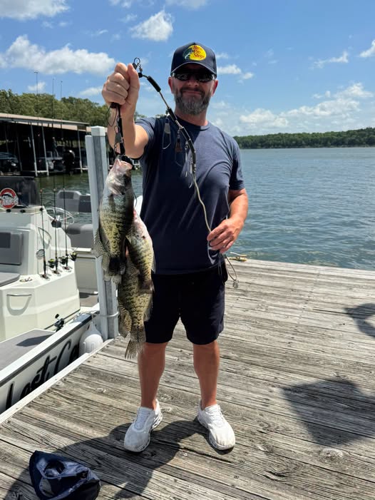 Angler displaying caught fish on wooden dock at Pittsburg MO marina with boat and lake in background