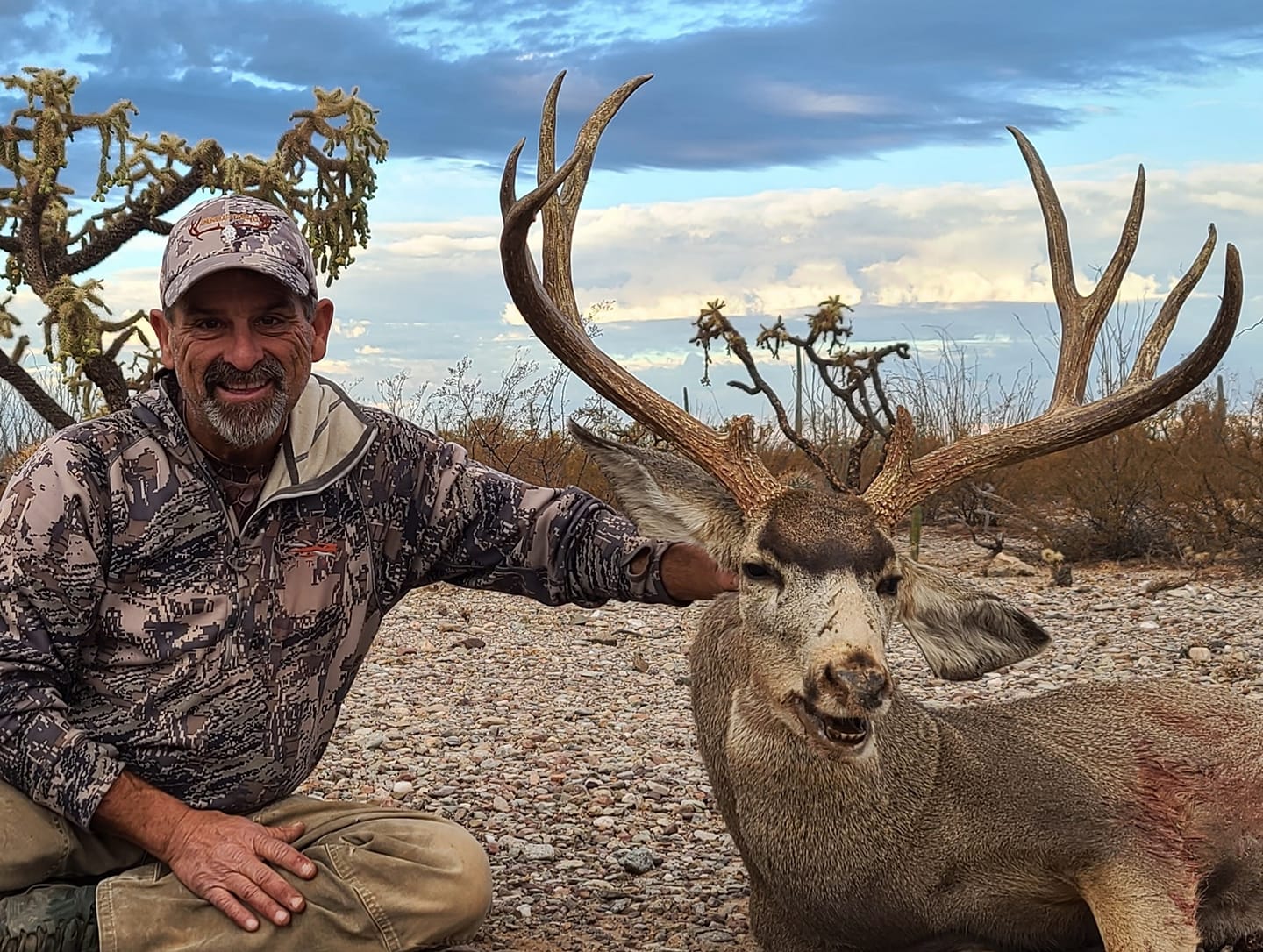 Hunter with harvested mule deer buck displaying large antler rack in desert landscape near Flagstaff Arizona