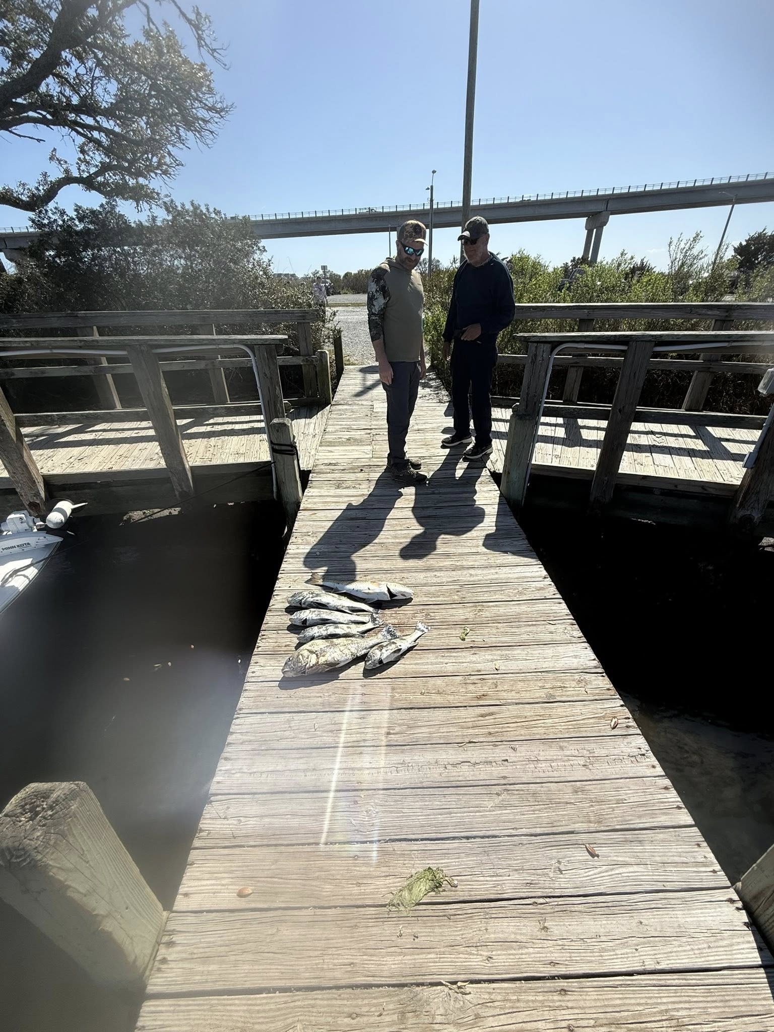 Two anglers standing on wooden fishing dock in Surf City NC with fresh caught fish displayed on planks