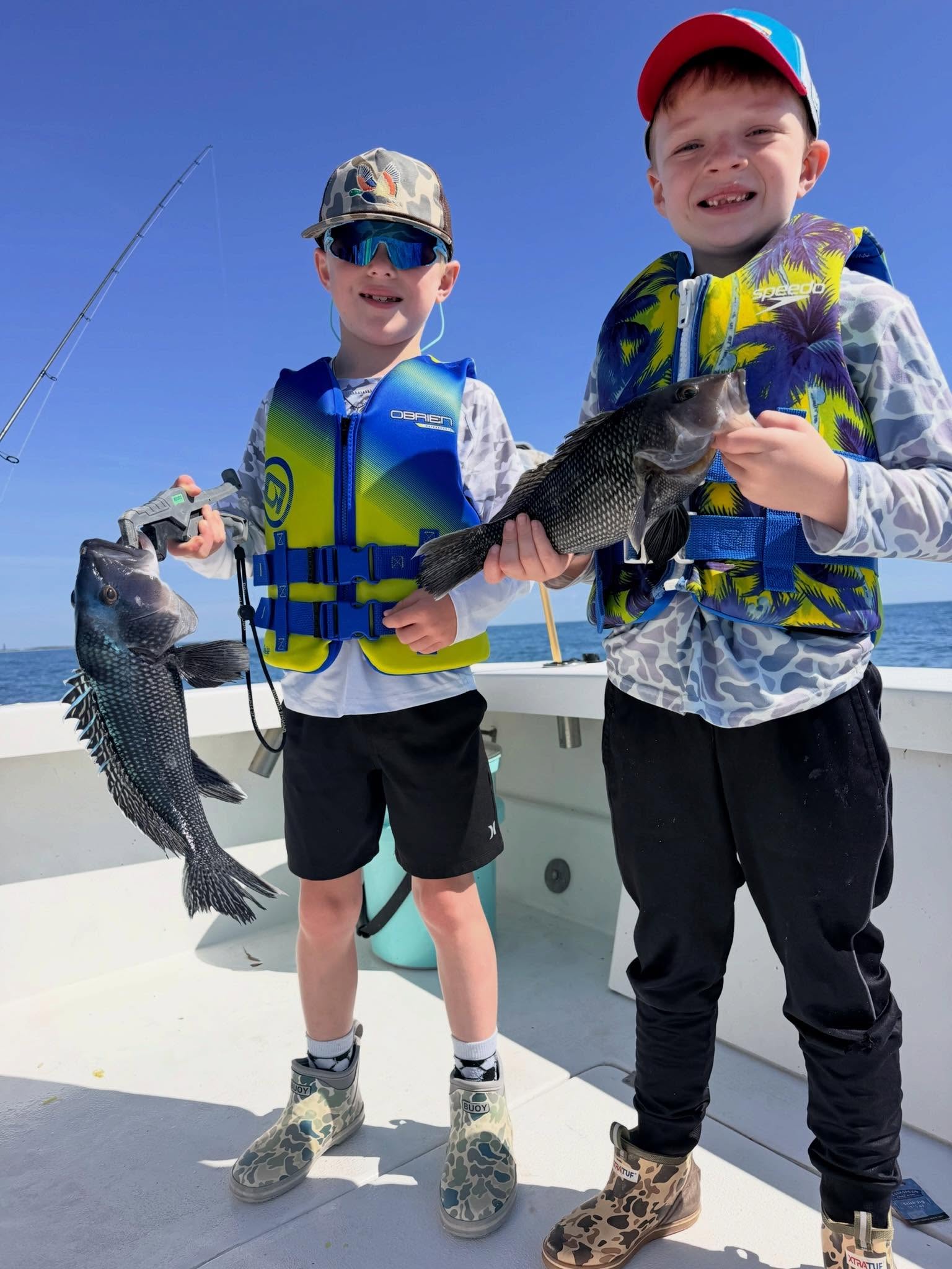 Two young anglers displaying caught black sea bass on fishing boat in Morehead City NC