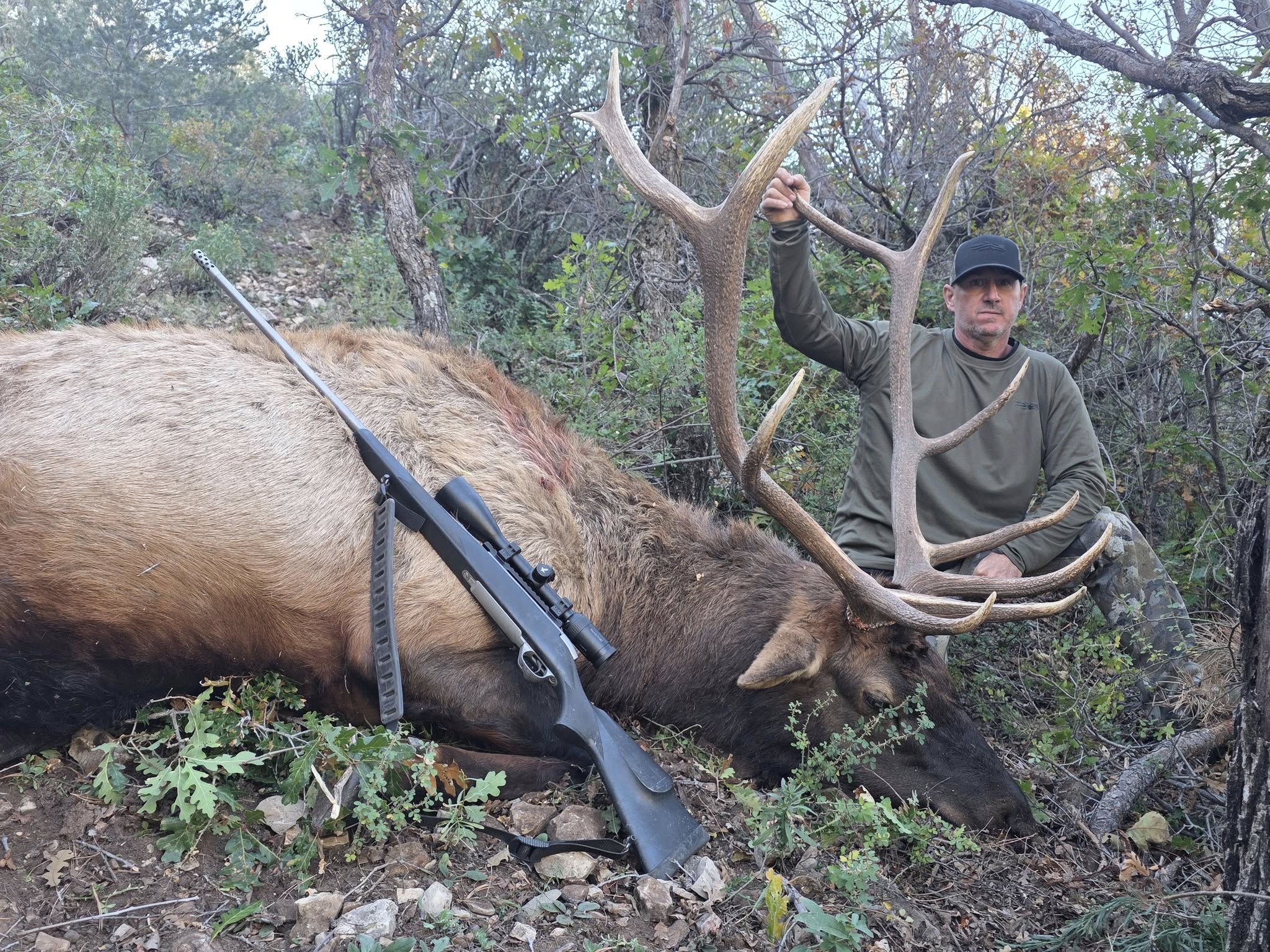 Hunter posing with harvested elk and rifle in Mayhill New Mexico wilderness