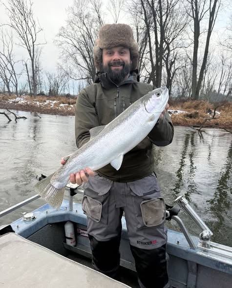Angler holding large fish while standing in boat on river in Manistee MI