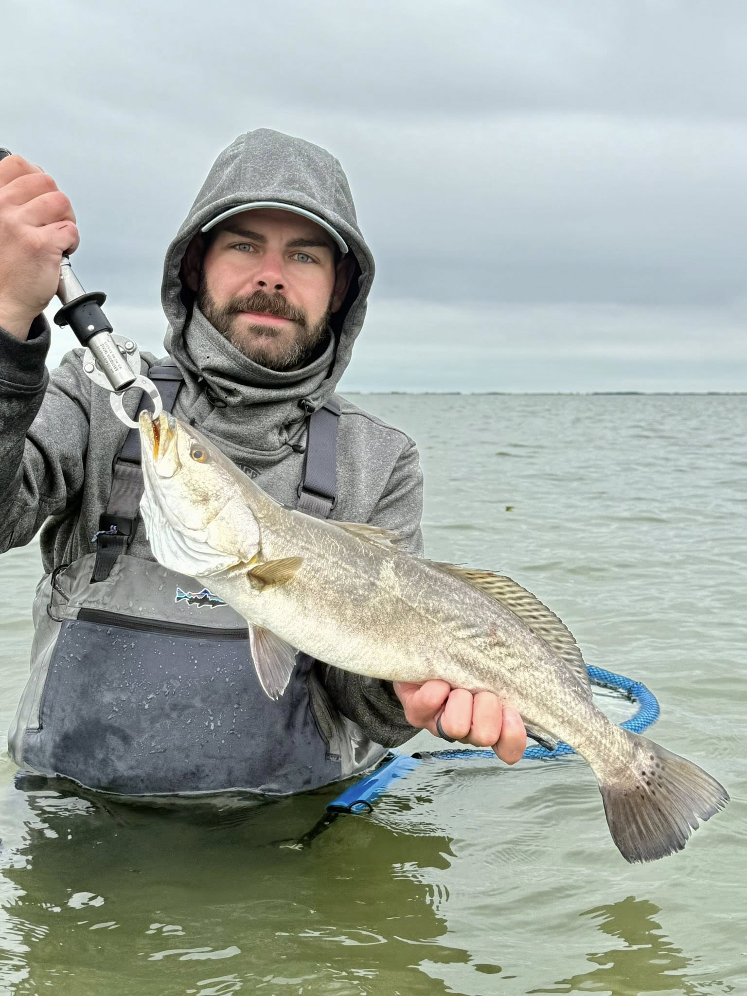 Angler holding speckled trout catch while wade fishing in shallow coastal waters near Riviera Texas