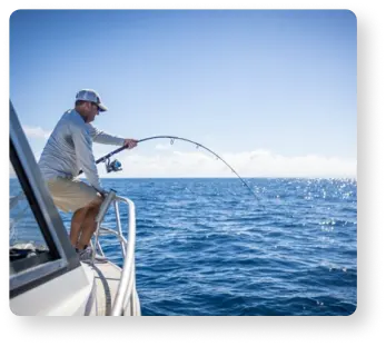 Book a trusted trip with Guidesly- A man holds a fishing rod at the edge of a boat in the ocean.